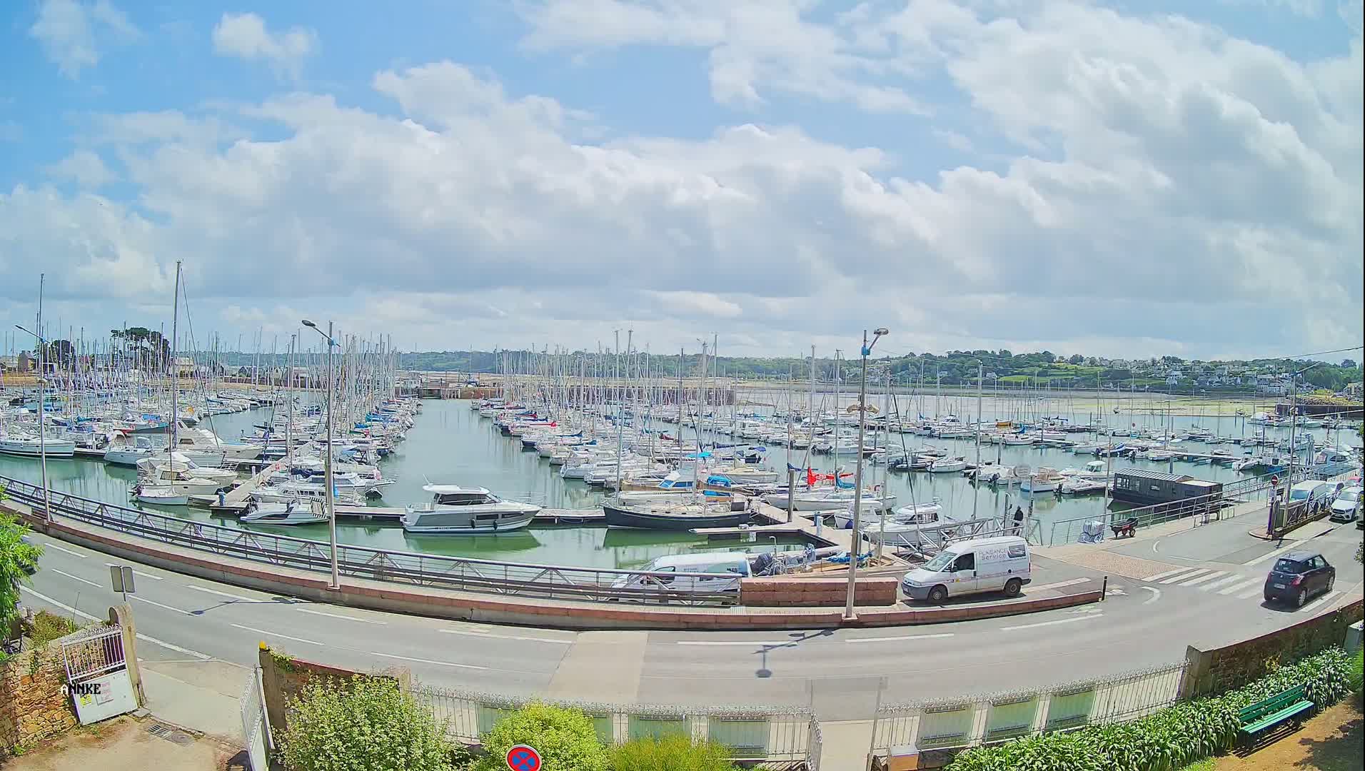 A marina filled with numerous sailboats and motorboats is visible under a partly cloudy sky.