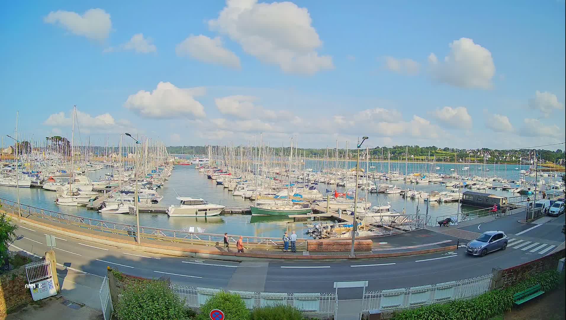 A marina filled with numerous sailboats and motorboats under a partly cloudy, sunny sky.