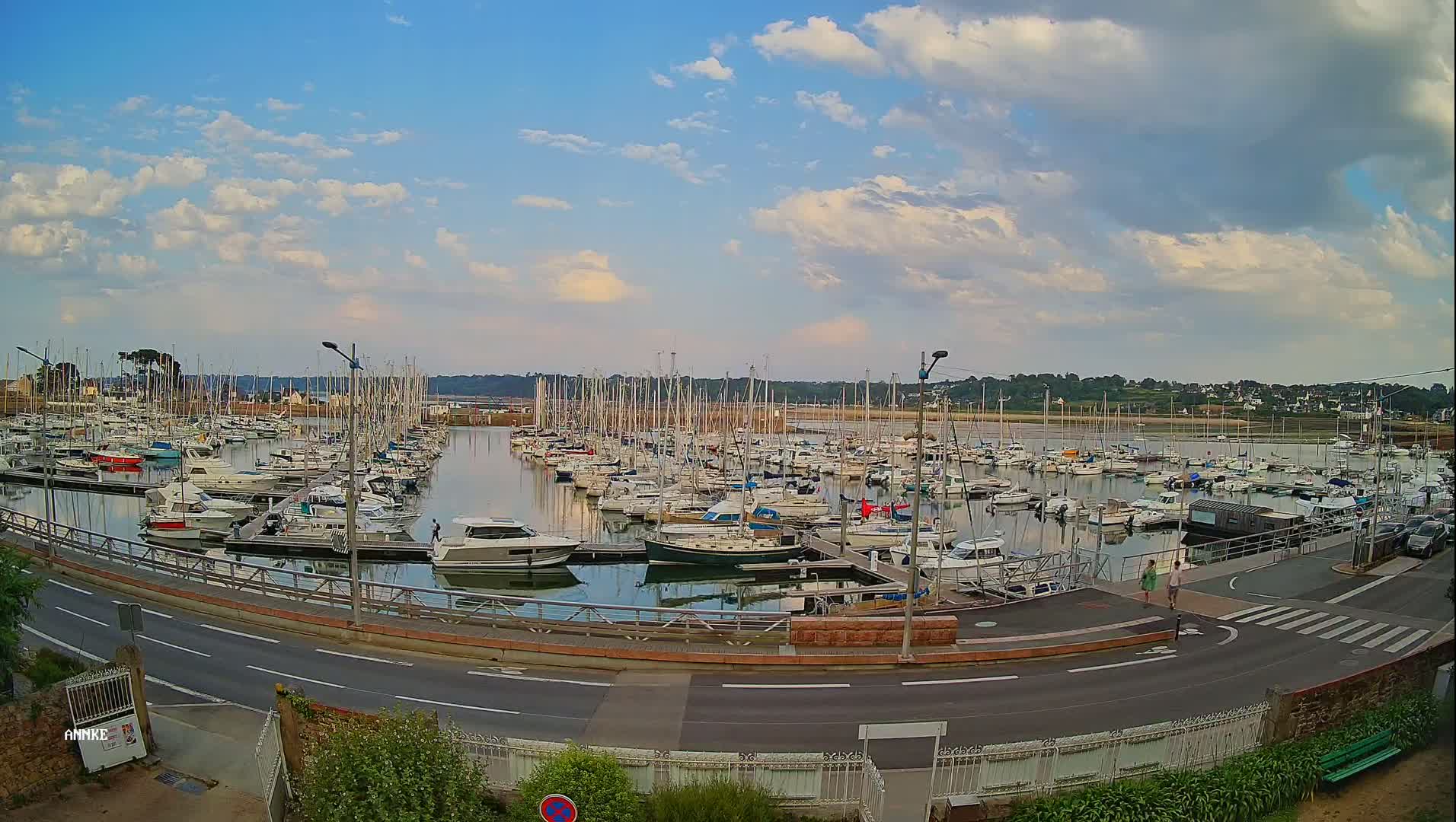 A marina filled with numerous sailboats and motorboats is seen under a partly cloudy sky.