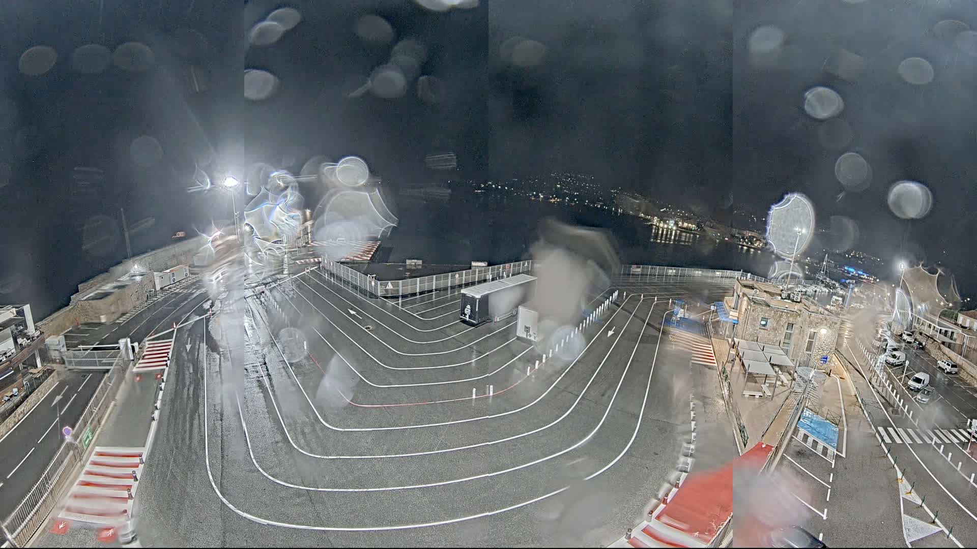 A wet, nighttime view of a ferry terminal with a large truck parked in the center, and marked lanes guiding vehicles.