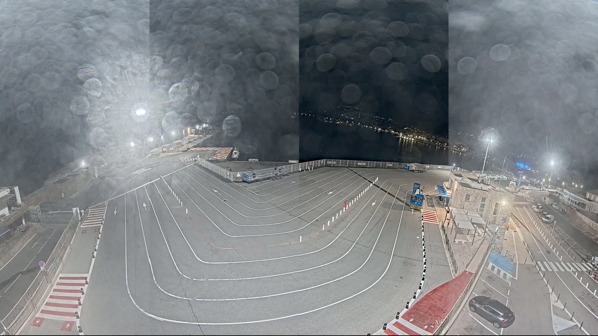 A nighttime view of a ferry terminal's vehicle queuing area, with a misty or rainy atmosphere and lights illuminating the scene.