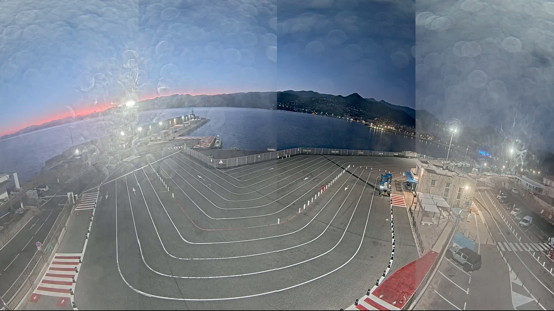 An empty ferry terminal with marked lanes curves toward a body of water under a twilight sky.