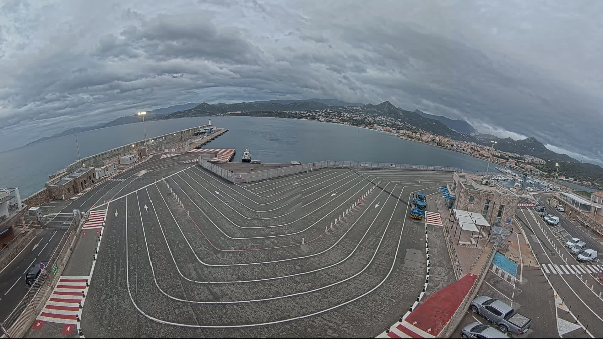 A ferry terminal with a large, curving roadway leading to a dock, under a cloudy sky.