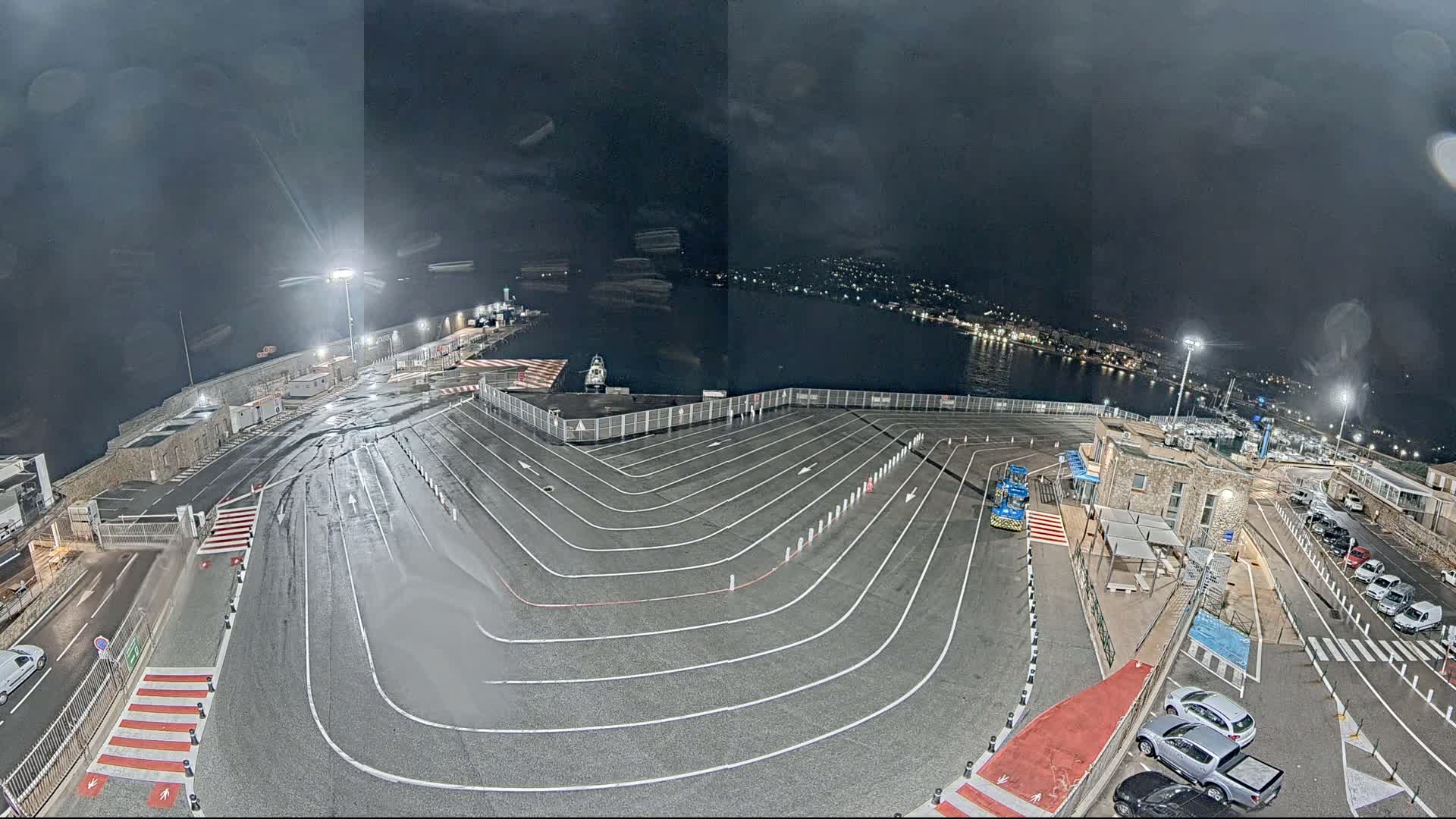 A wet, nighttime view of a ferry terminal with marked vehicle lanes and a few cars parked near the building.