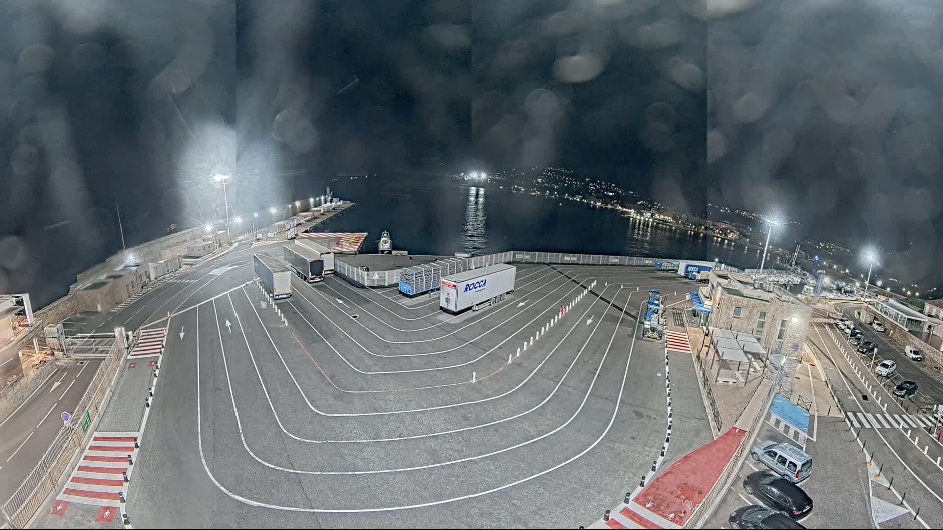A nighttime view of a ferry terminal with several trucks parked, under a cloudy sky.