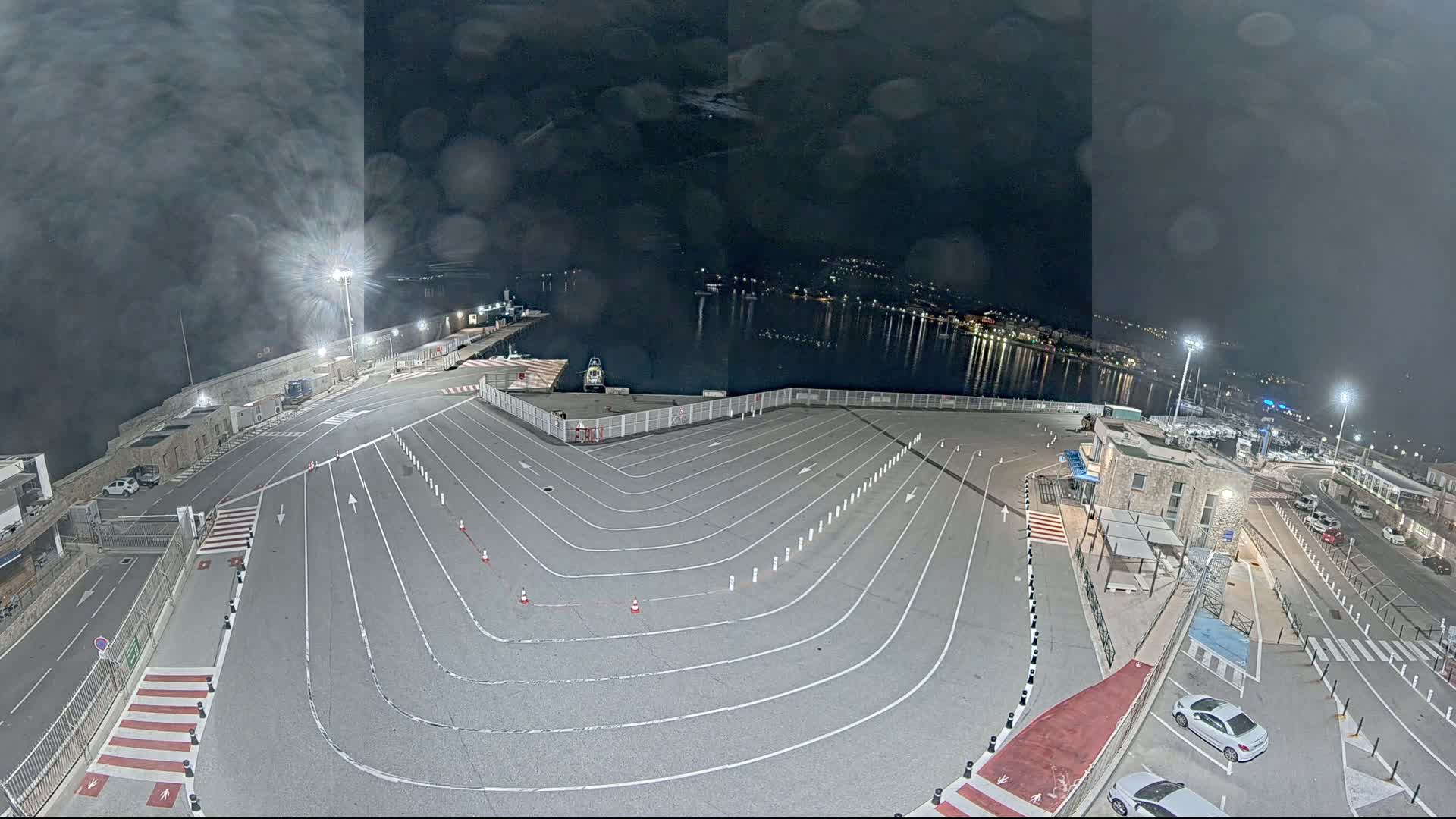 An empty, marked parking lot at a harbor at night under a cloudy sky.