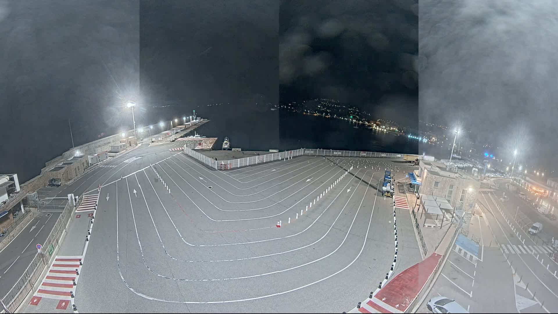 An empty, marked parking lot at a harbor at night, under a hazy, dark sky.