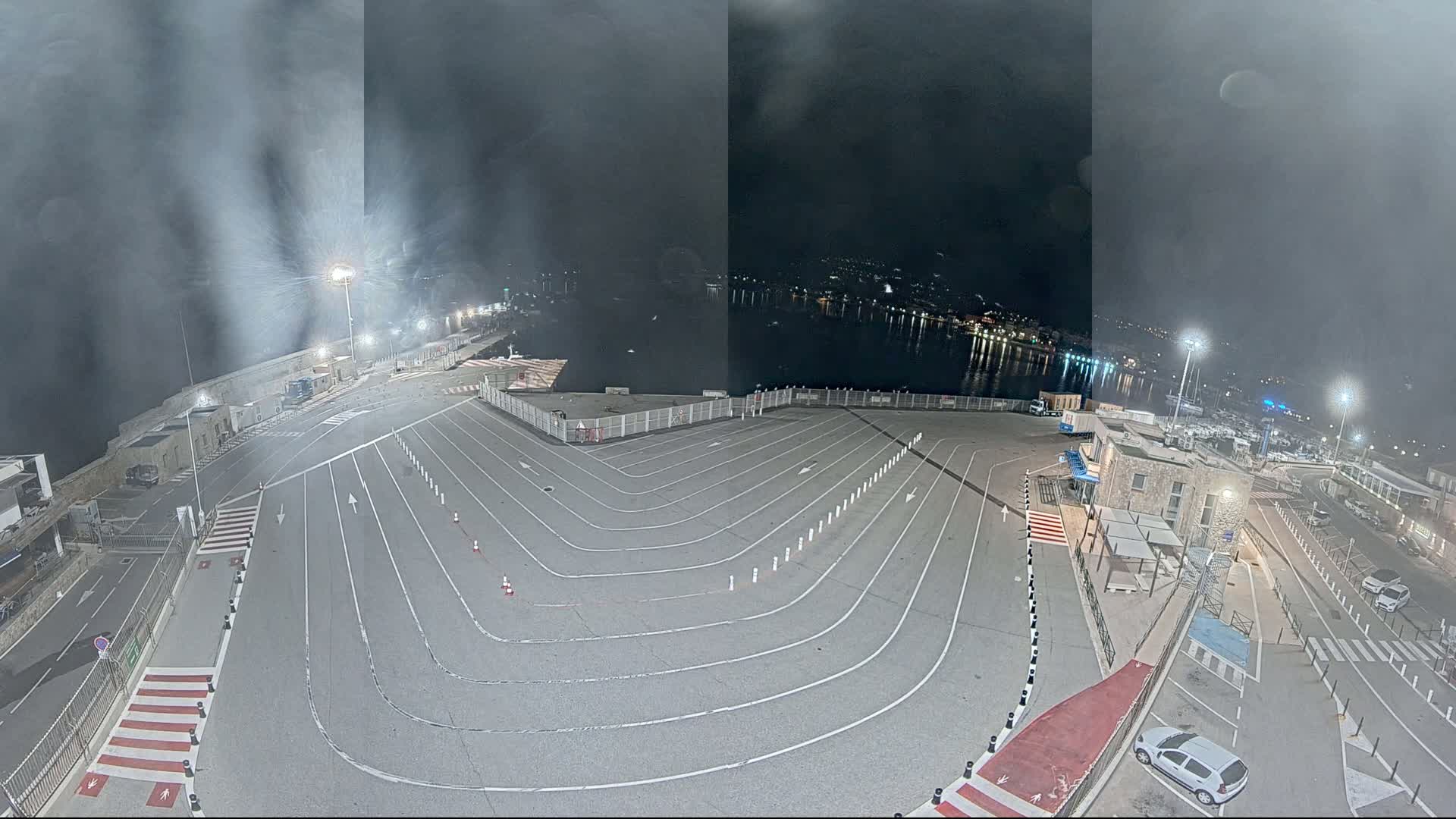 An empty, marked parking lot at a waterfront location at night, under hazy or foggy conditions.