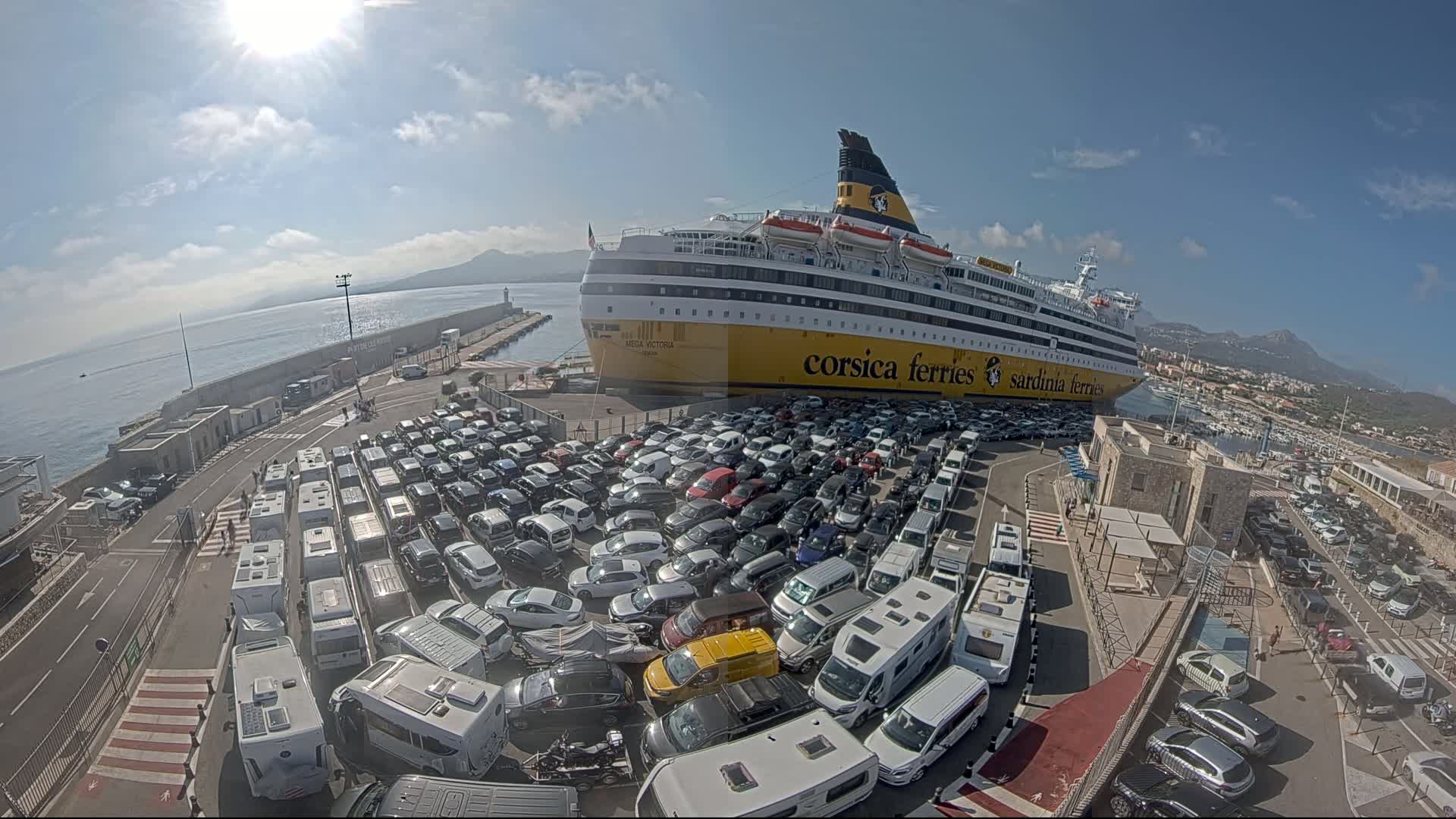 A large ferry is docked at a port on a sunny day, surrounded by a large parking lot filled with cars and RVs.