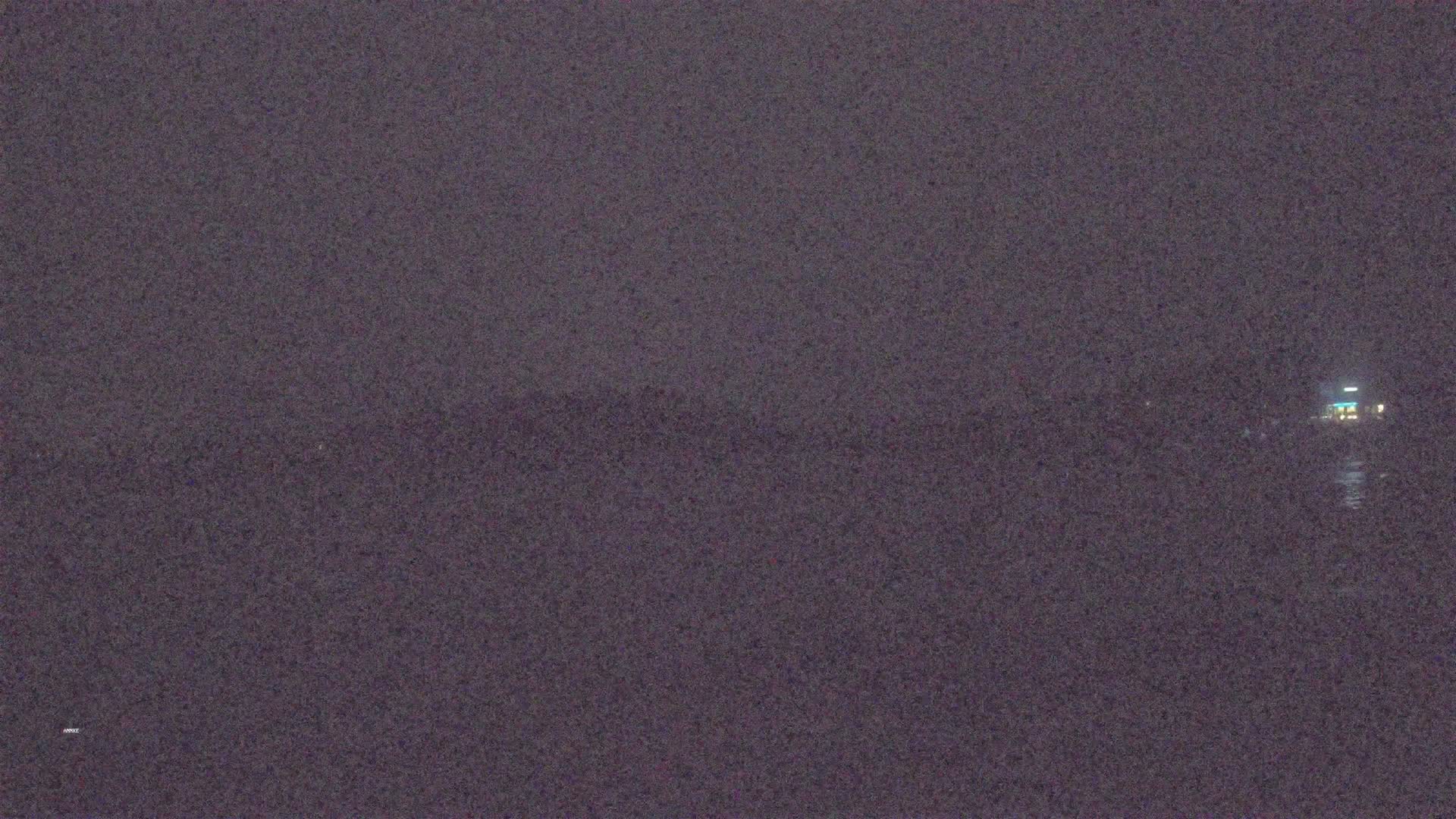 A dimly lit, dark body of water is shown at night with a faintly visible structure in the distance.