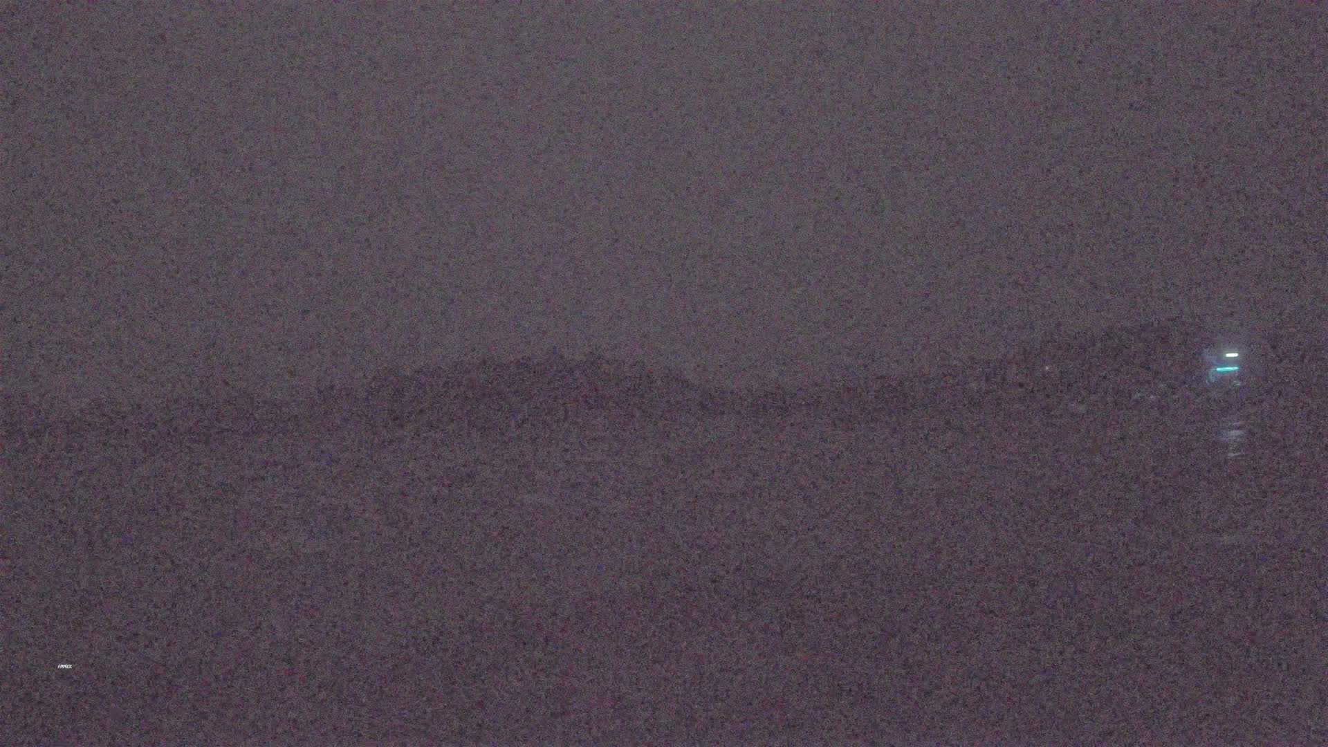 A blurry, dark image shows a distant, indistinct shoreline at night under a hazy sky.