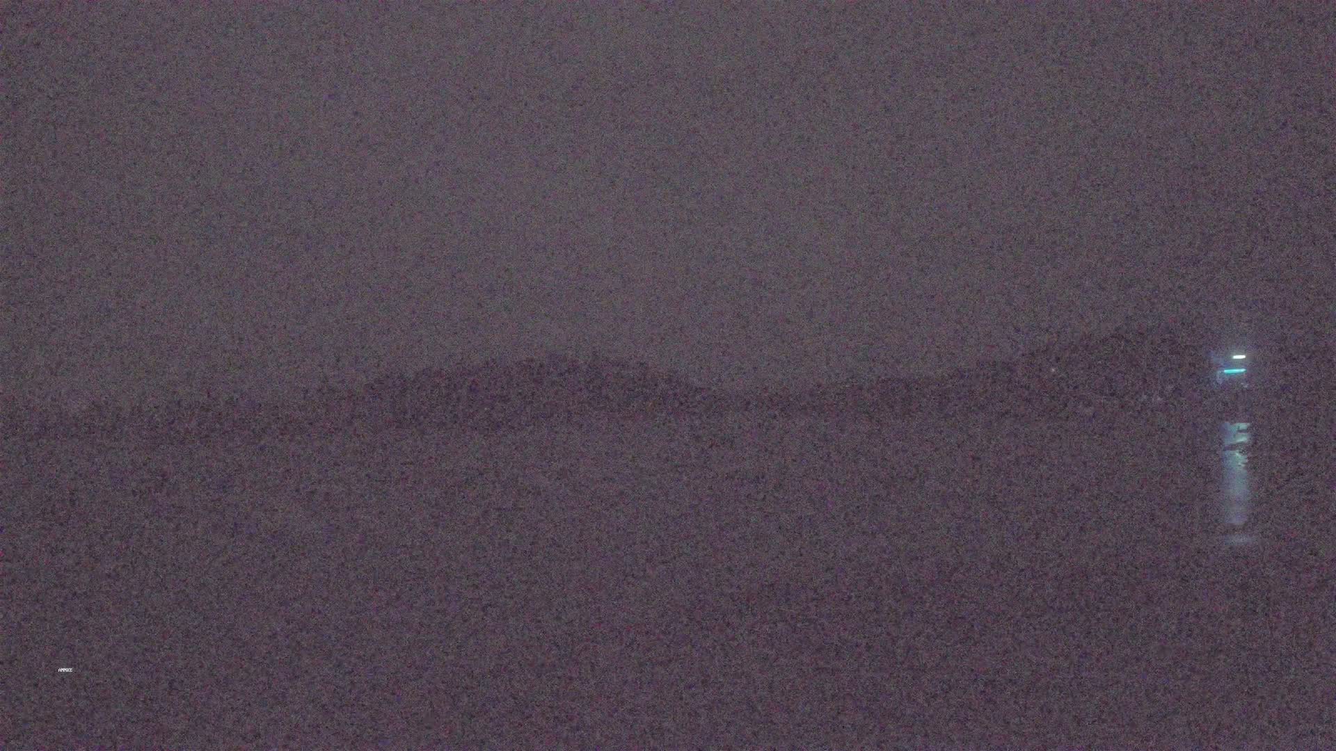 A dark, hazy nighttime scene shows a distant, indistinct shoreline with a small light visible on the right.