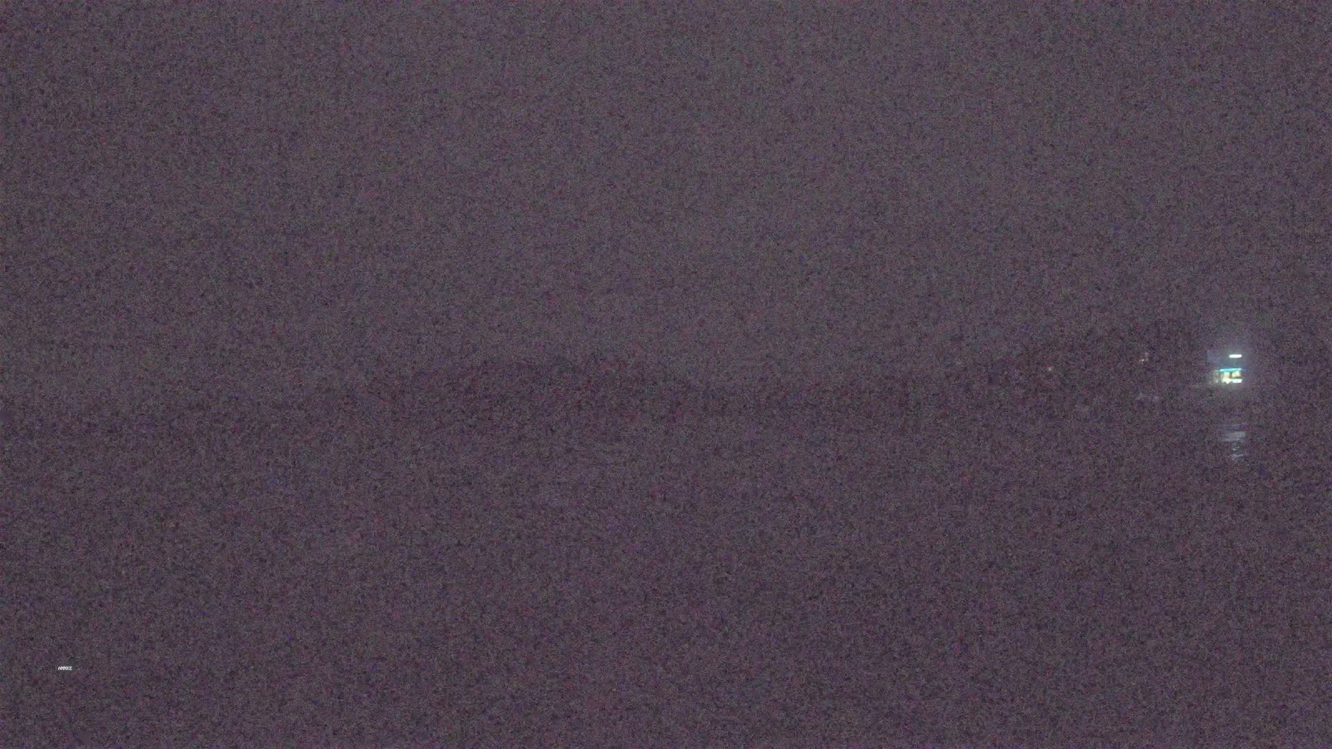 A dark, blurry nighttime image shows a dimly lit structure across a body of water under a dark sky.