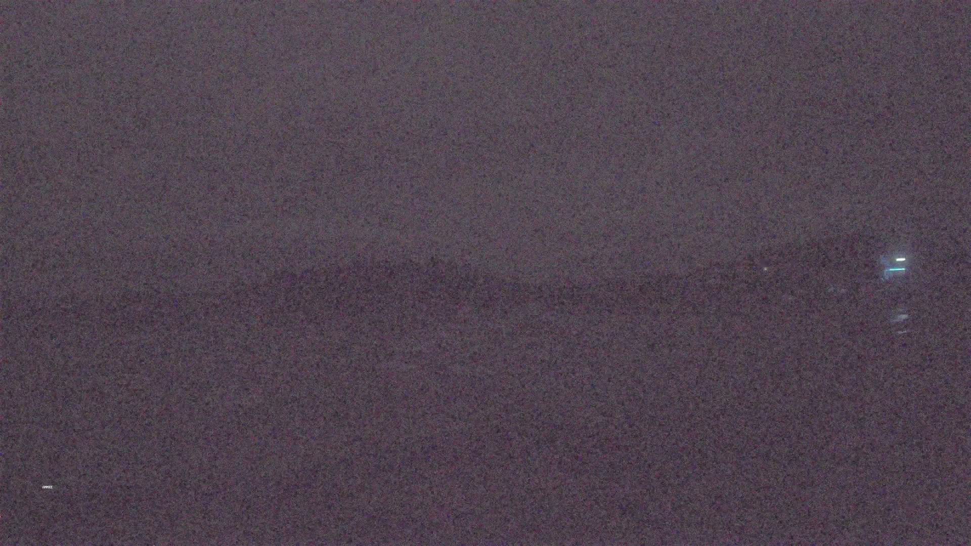 A blurry, dark image shows a distant, indistinct shoreline at night under a hazy sky.