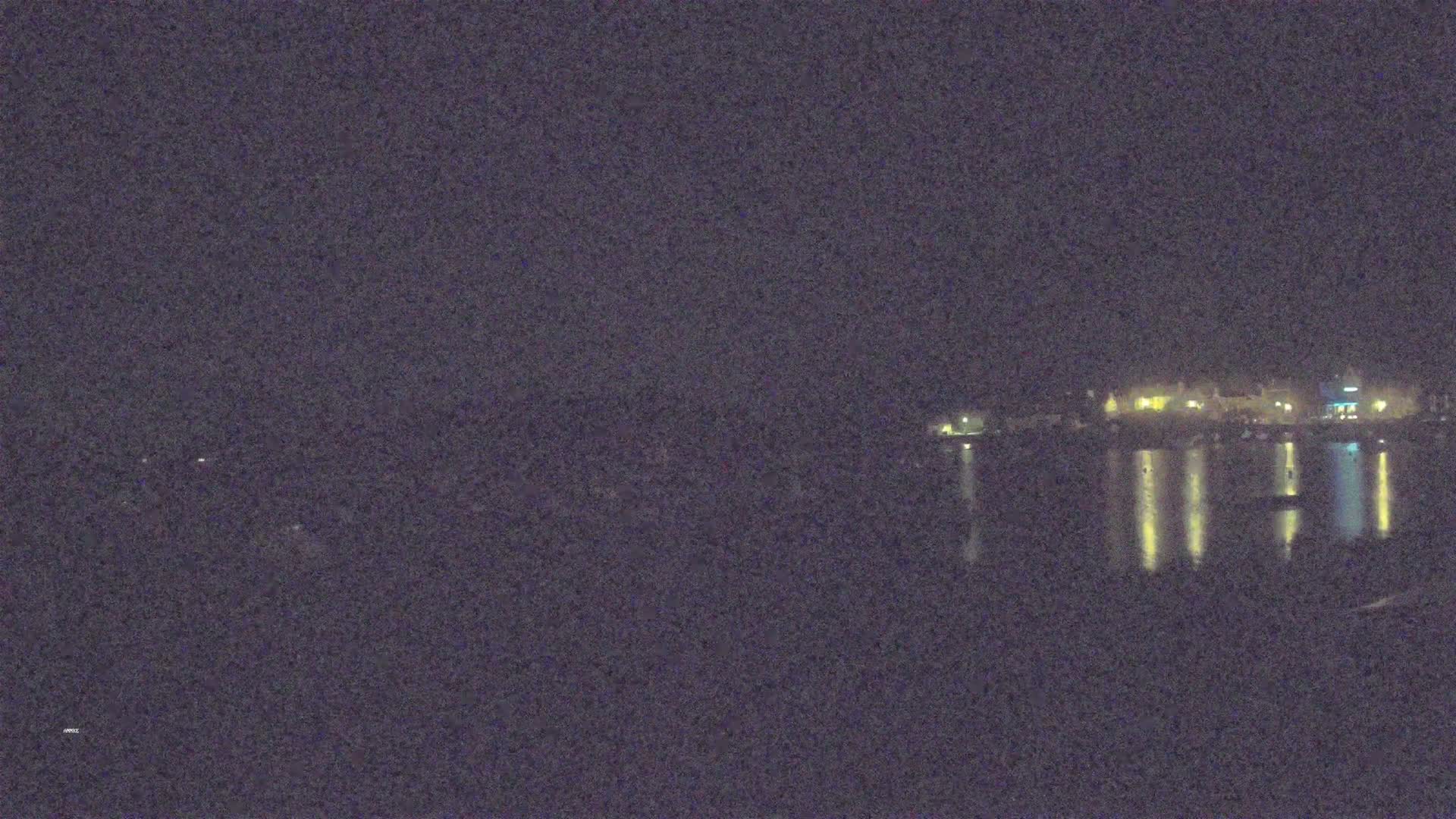 A nighttime view of a town's lights reflected on calm water.