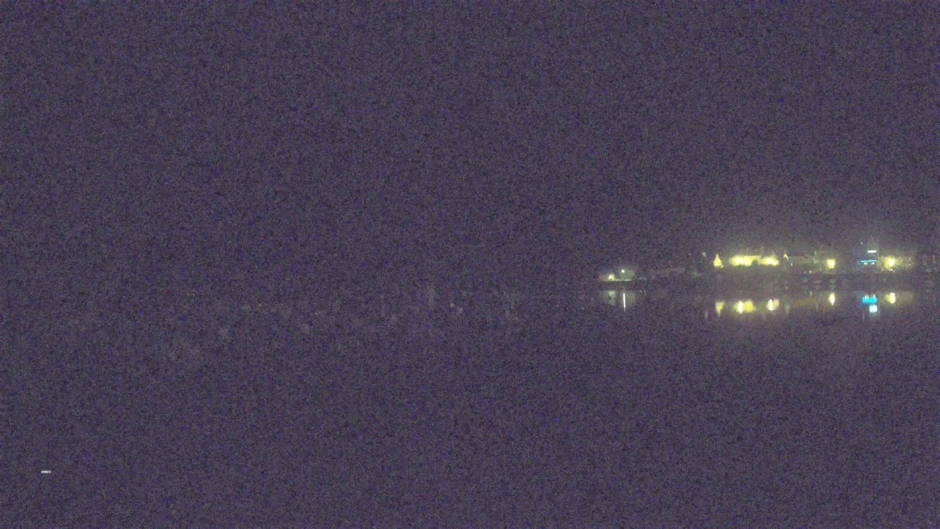 A nighttime view of a calm body of water reflecting the lights of a distant town under a dark sky.