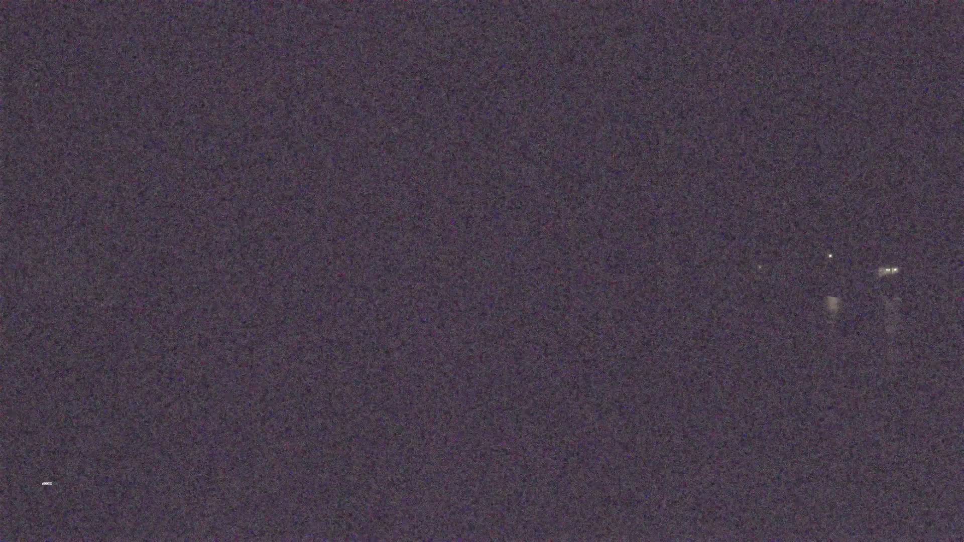A dark, nighttime scene shows a few faint lights in the distance.