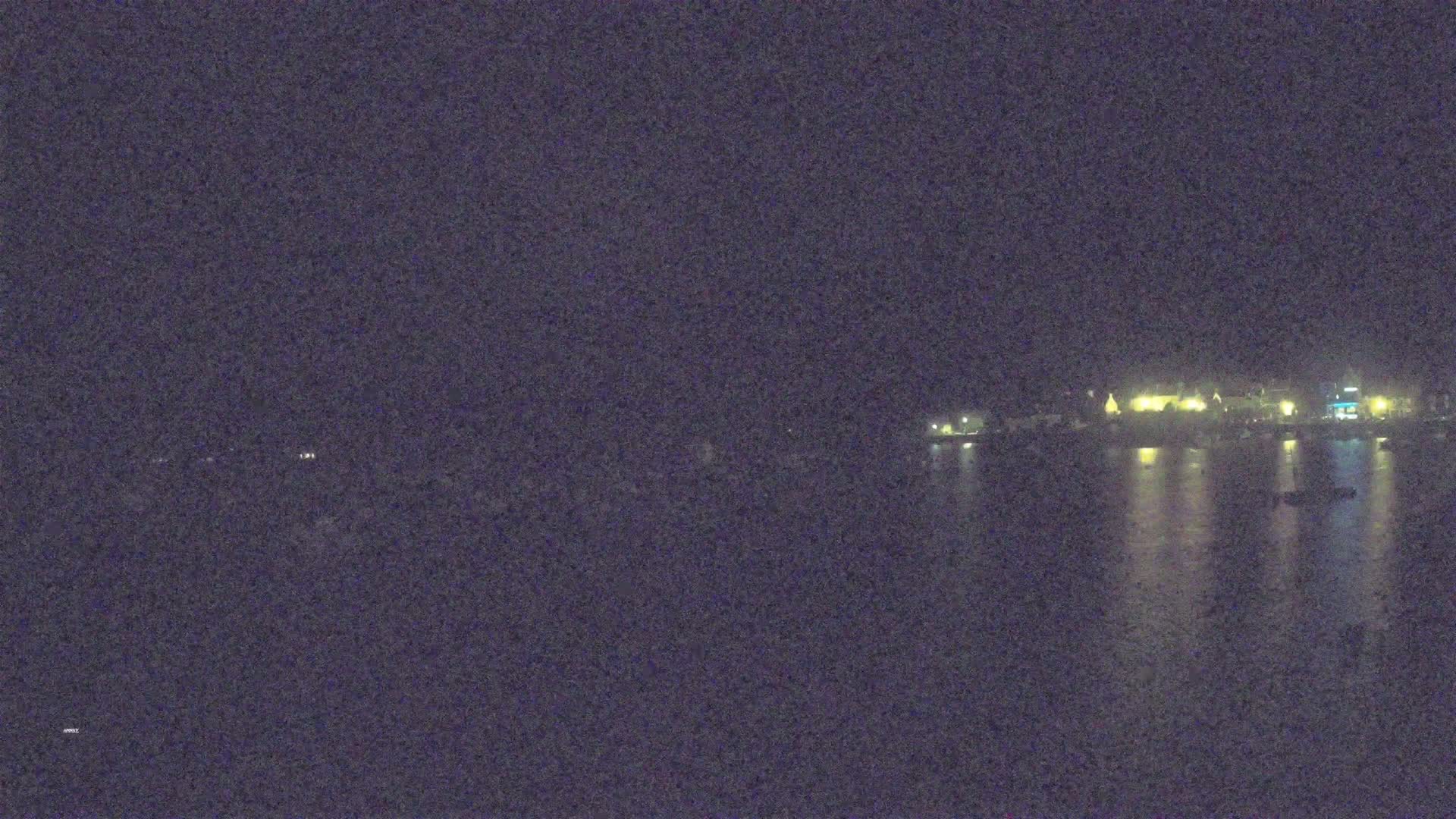 A nighttime view of a calm body of water reflecting the lights of a distant town under a dark sky.