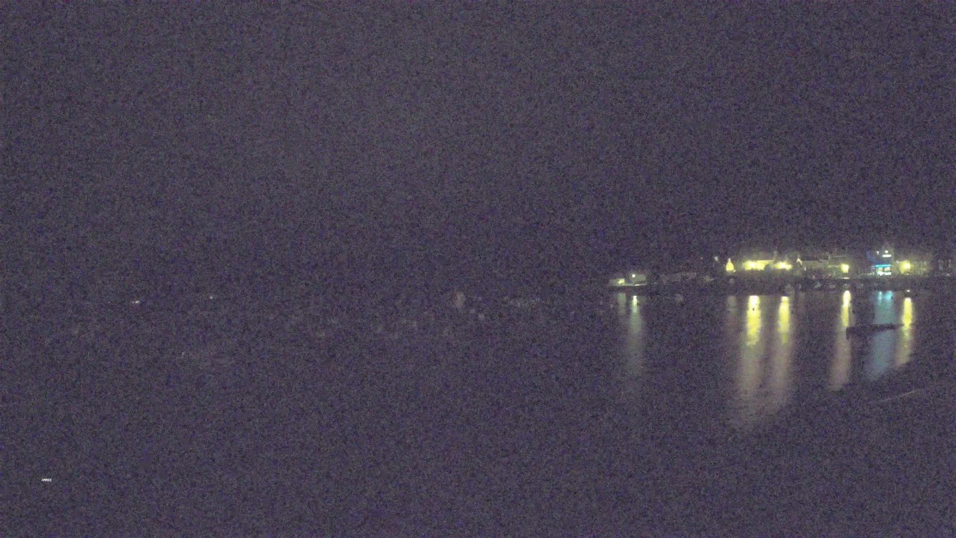 A nighttime, low-light view of a waterfront town with lights reflecting on the calm water.