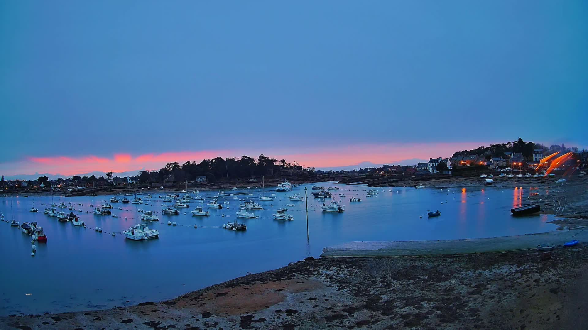 Many small boats are moored in a calm bay at dusk under a pale pink and blue sky.