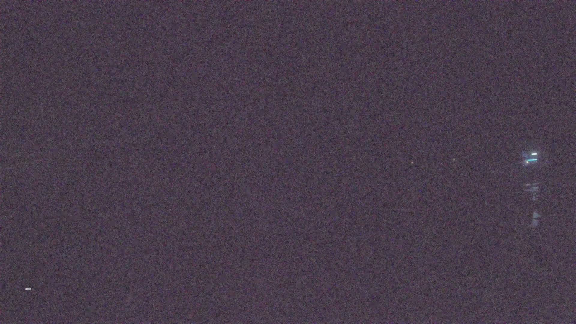 A dark, grainy nighttime image shows a few faint lights in the distance.