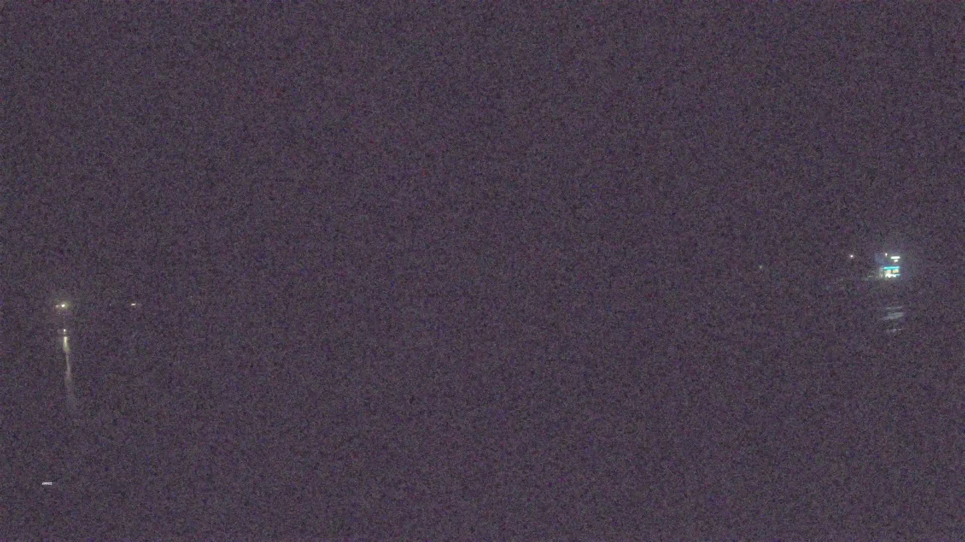 A nighttime long shot shows a dark, possibly asphalt, surface with faint lights in the distance under a dark sky.