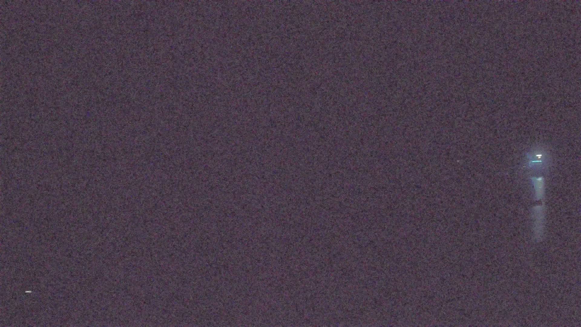 A dimly lit, dark-purple scene shows a single, faint light in the distance at night.