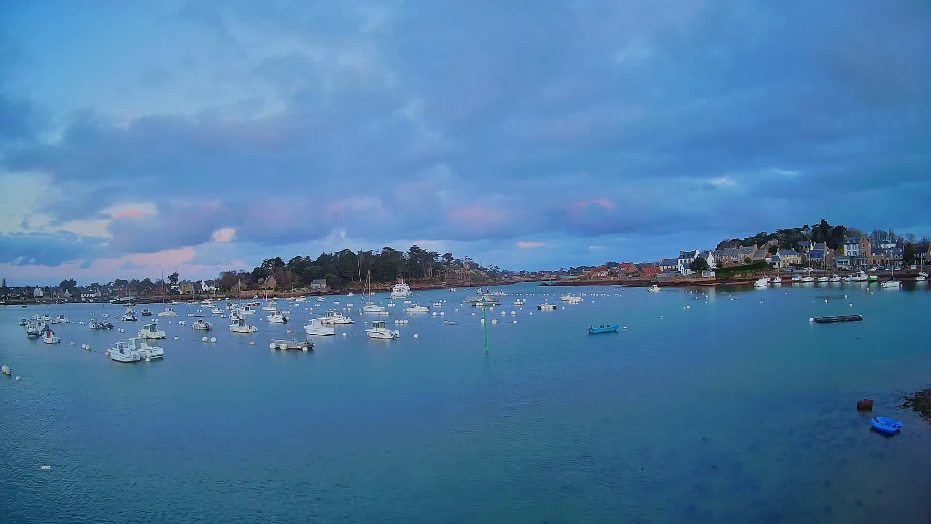 Numerous small white boats are moored in a calm, blue-green harbor under a partly cloudy, dusky sky.