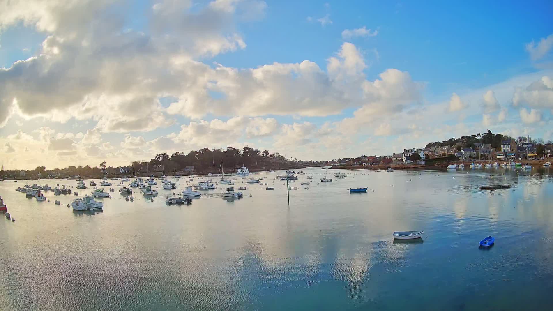 A calm bay with numerous small boats at anchor under a partly cloudy sky.