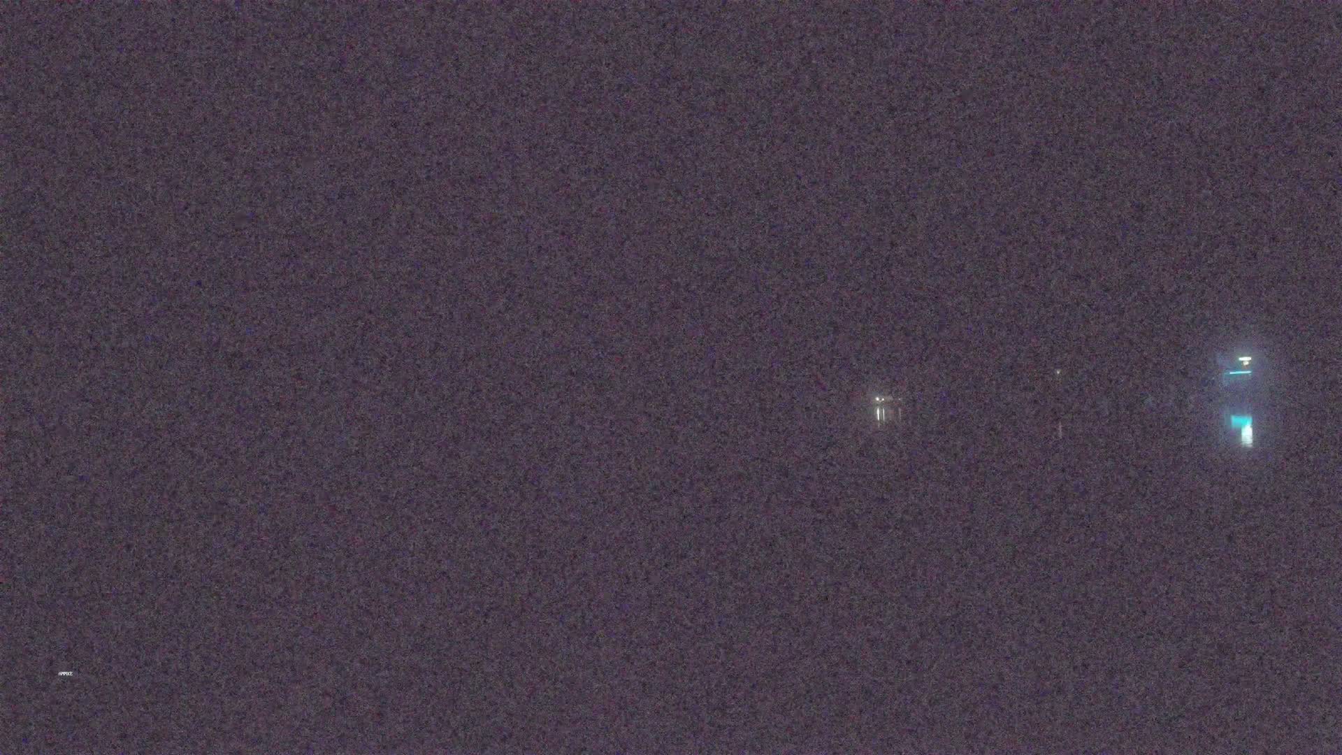 A nighttime image shows a few faint lights in the distance across a dark, blurry expanse.