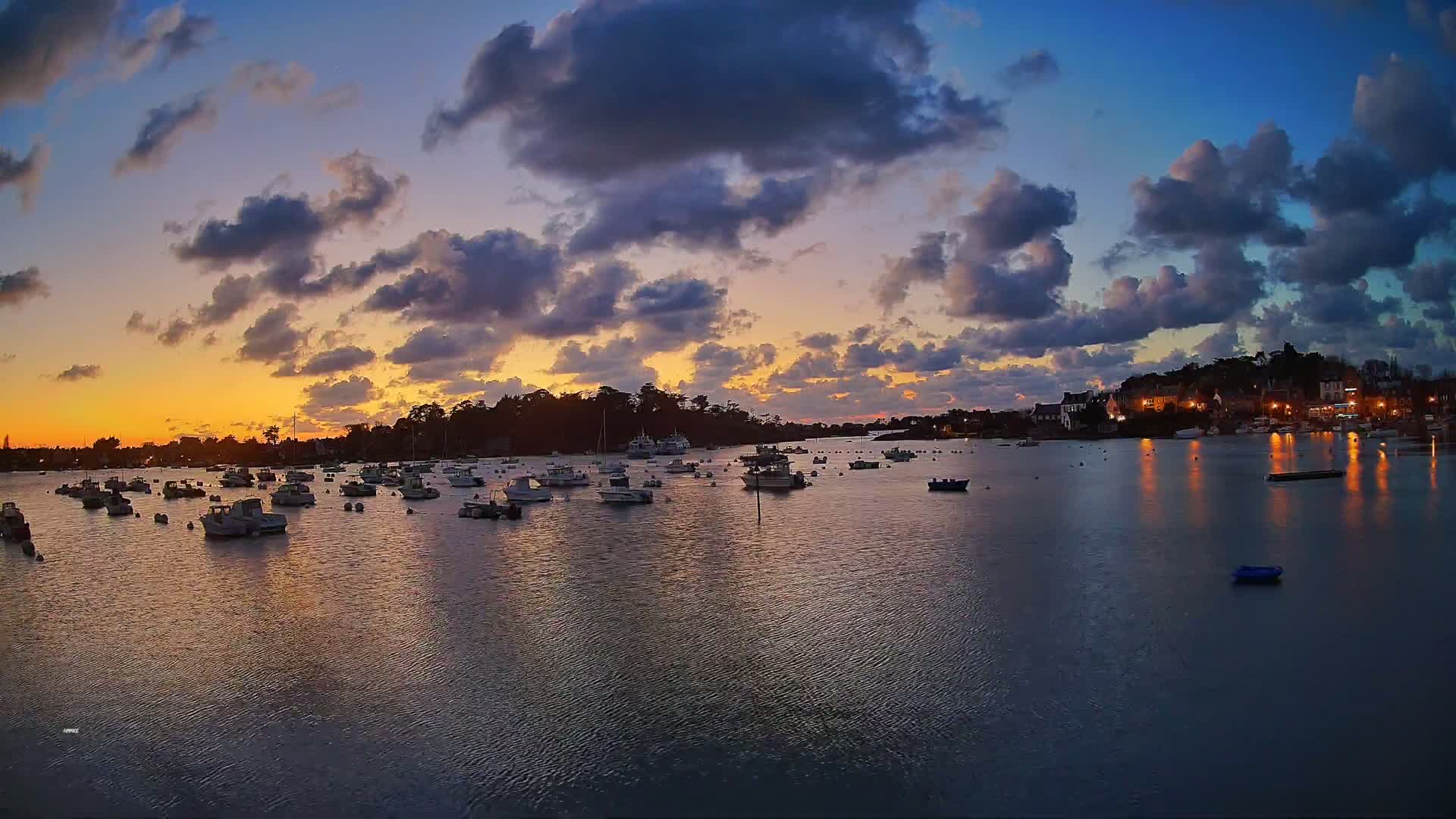 Many small boats are moored in a calm harbor at sunset under a partly cloudy sky.