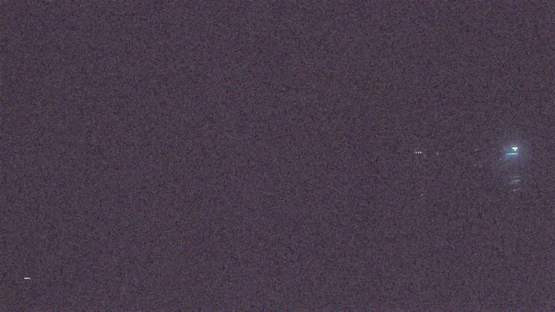 A nighttime, low-light image shows a dark, blurry scene with a few faint lights in the distance.