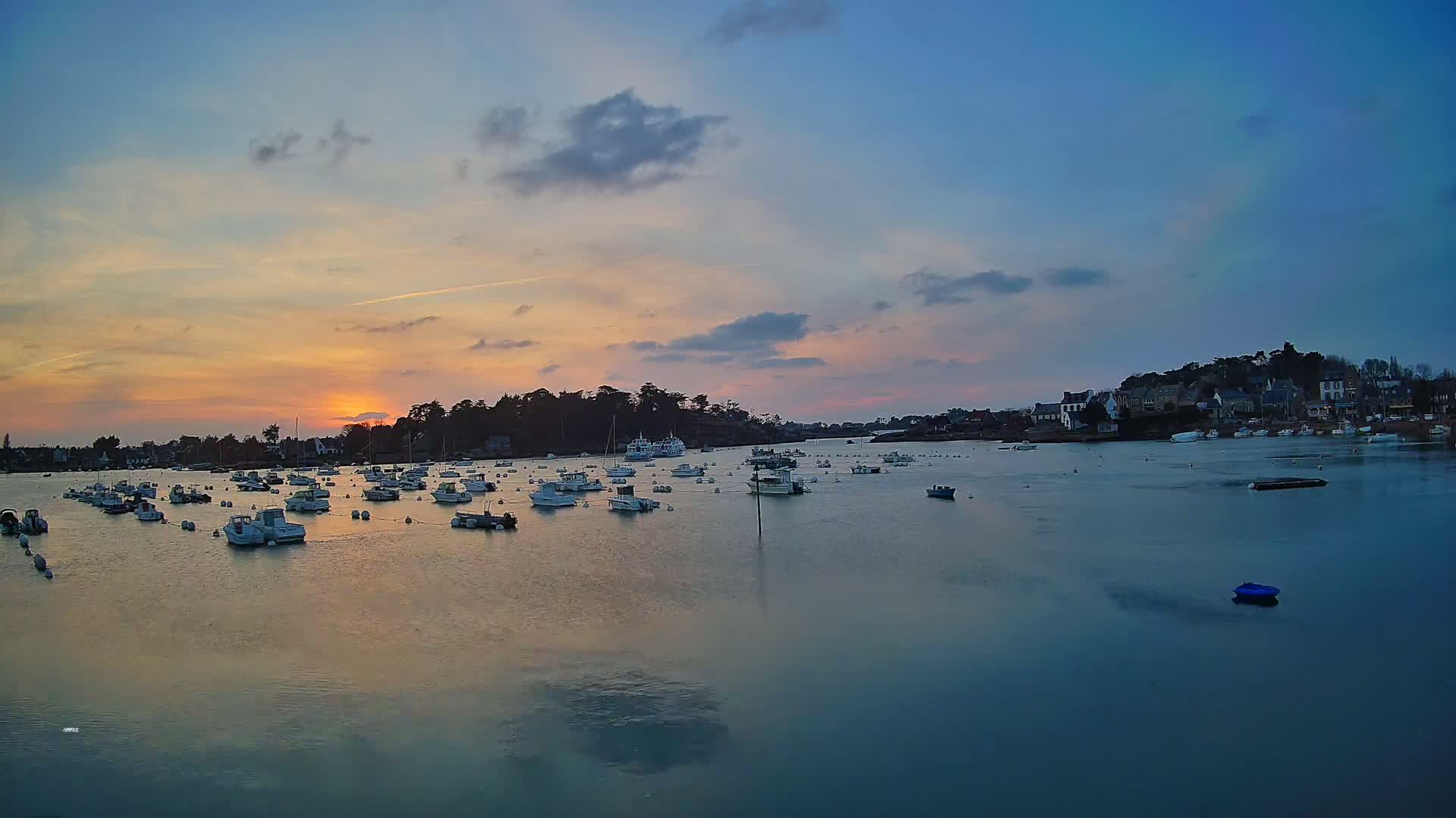 Many small boats are moored in a calm bay at sunset under a partly cloudy sky.