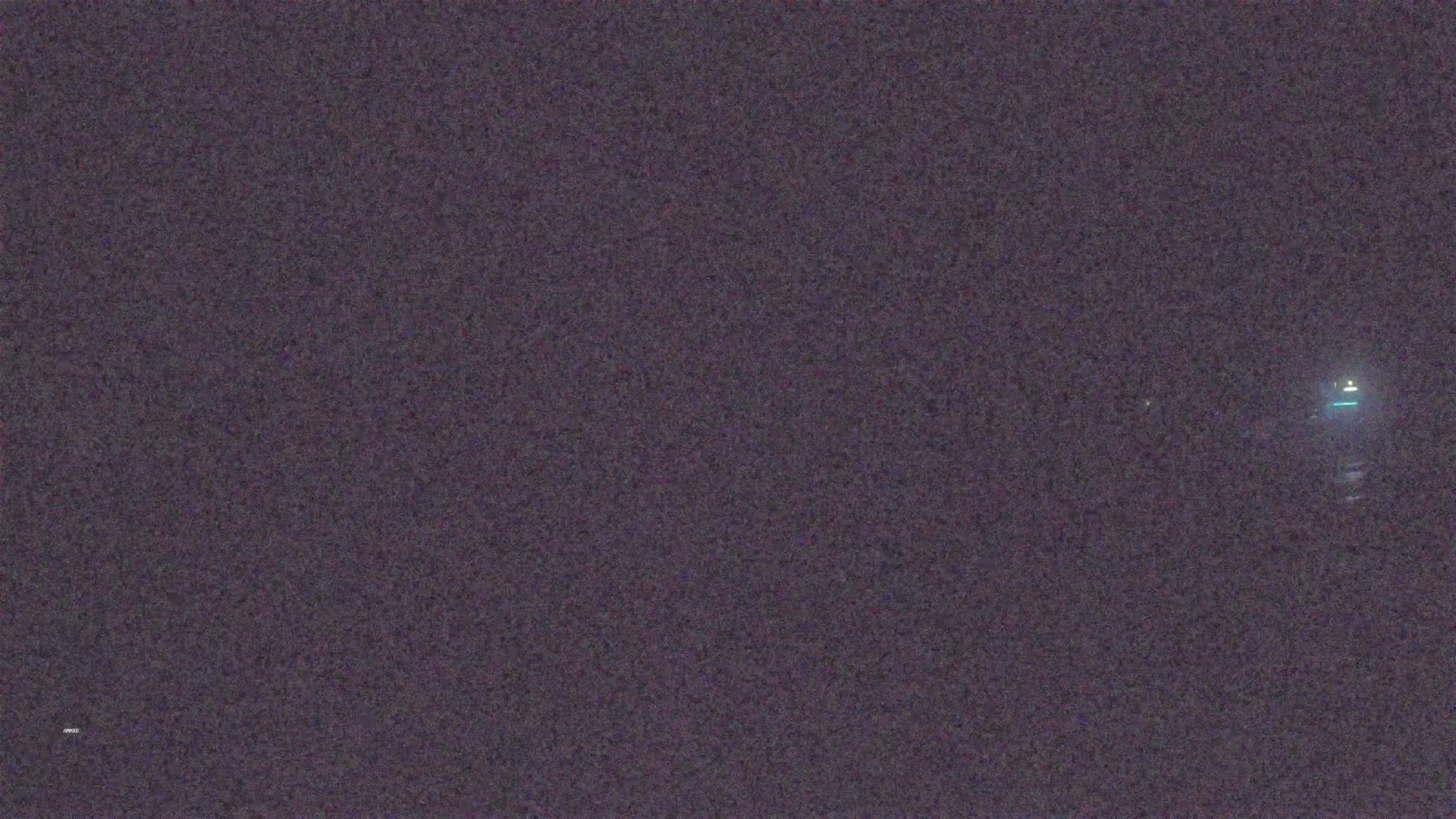 A dark, grainy image shows a small, indistinct light source in the distance at night.