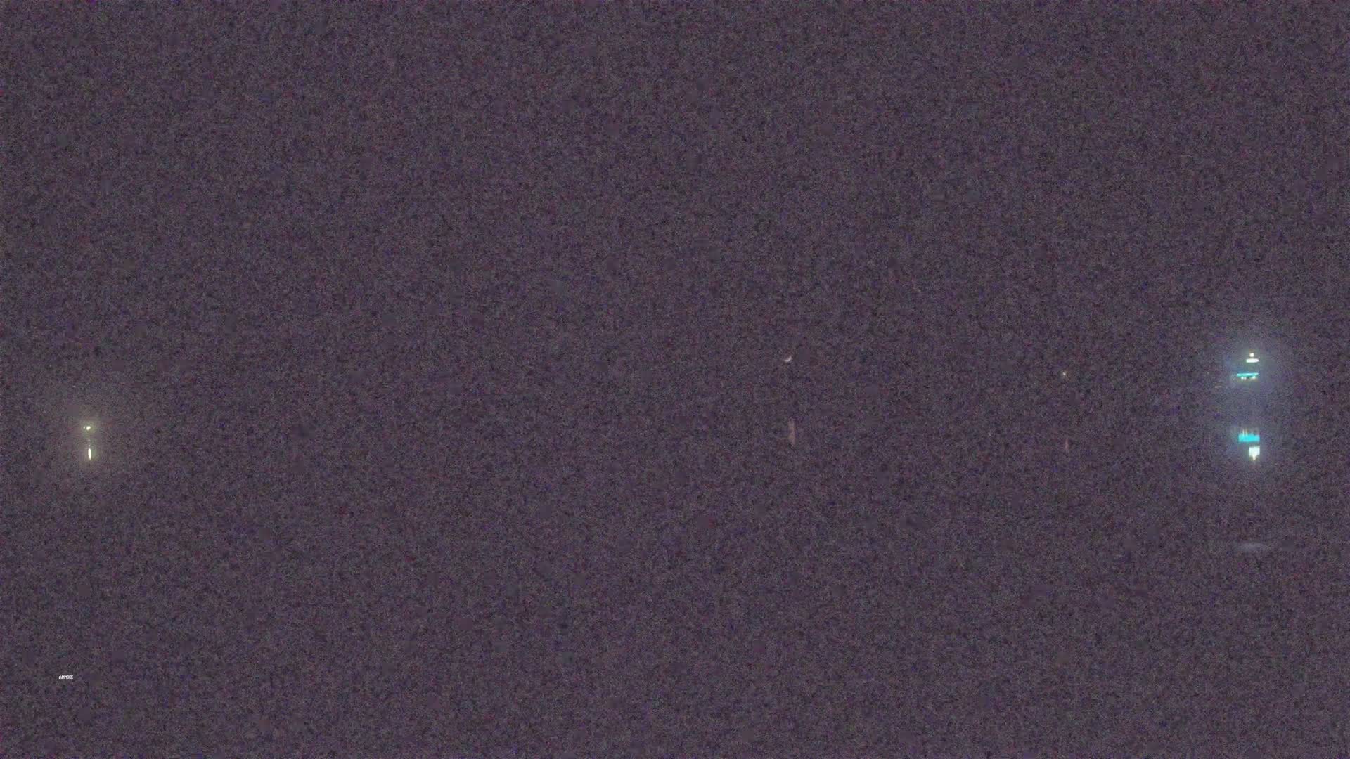 A dark, nighttime scene shows faintly lit structures in the distance.