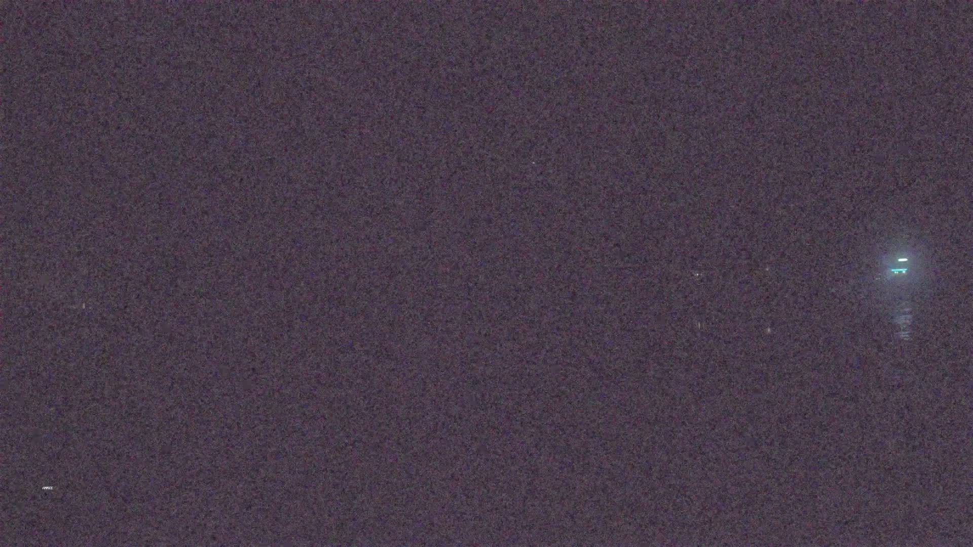 A blurry, nighttime image shows a dimly lit area with a faint light source in the distance.