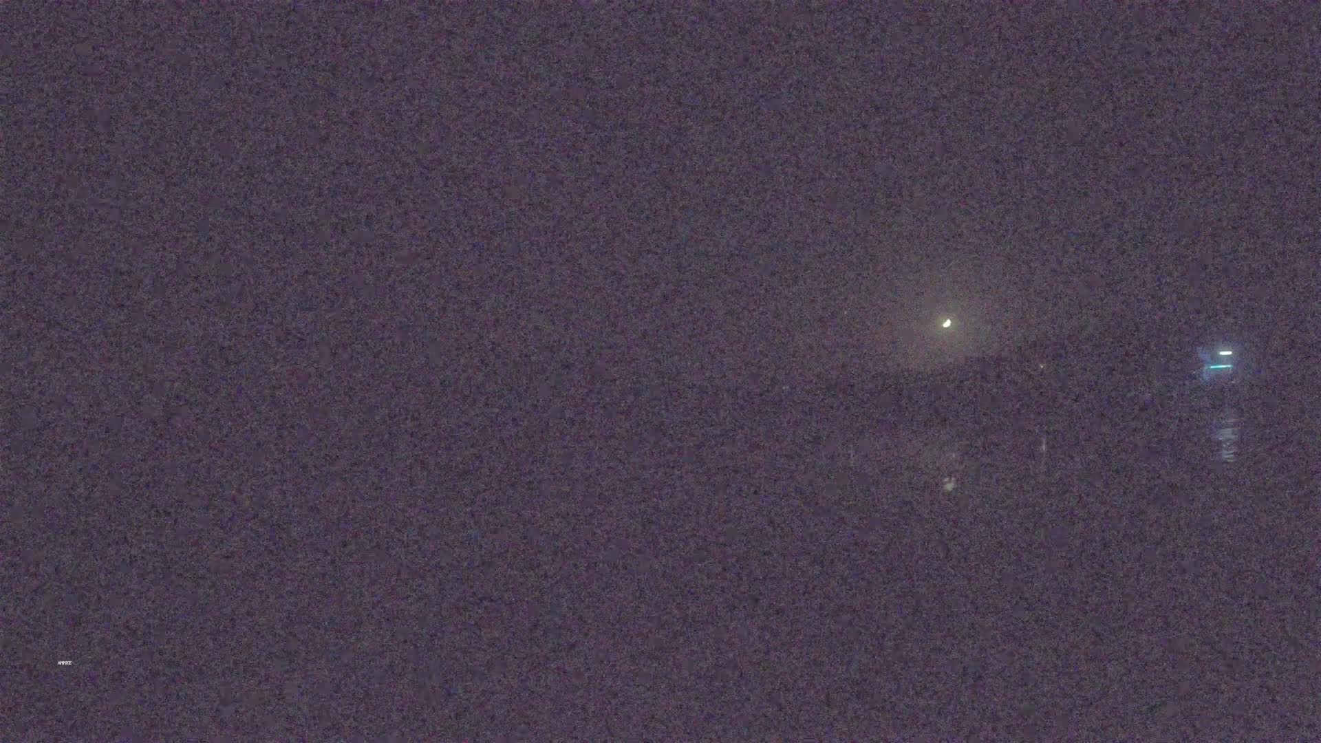 A nighttime view of a dark body of water under a slightly hazy sky with a crescent moon visible.