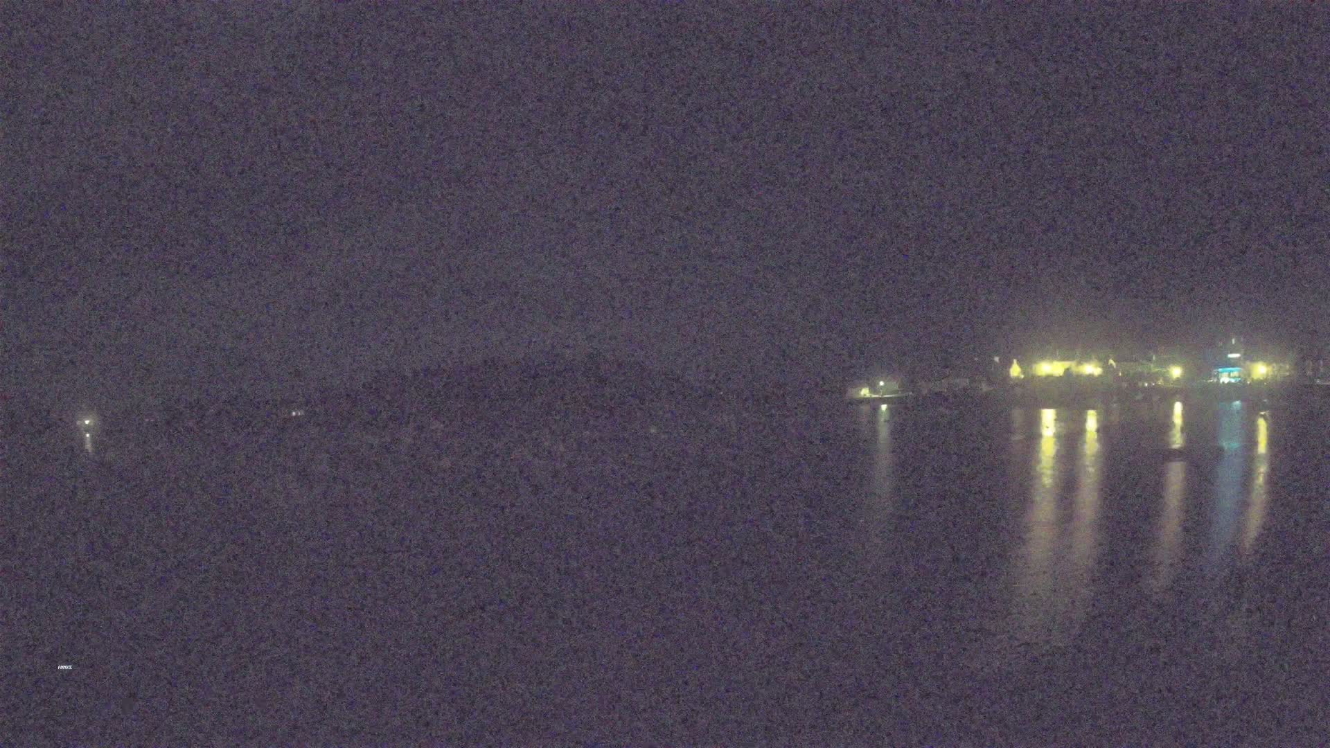 A nighttime view of a calm body of water reflecting the lights of a distant town under a dark sky.
