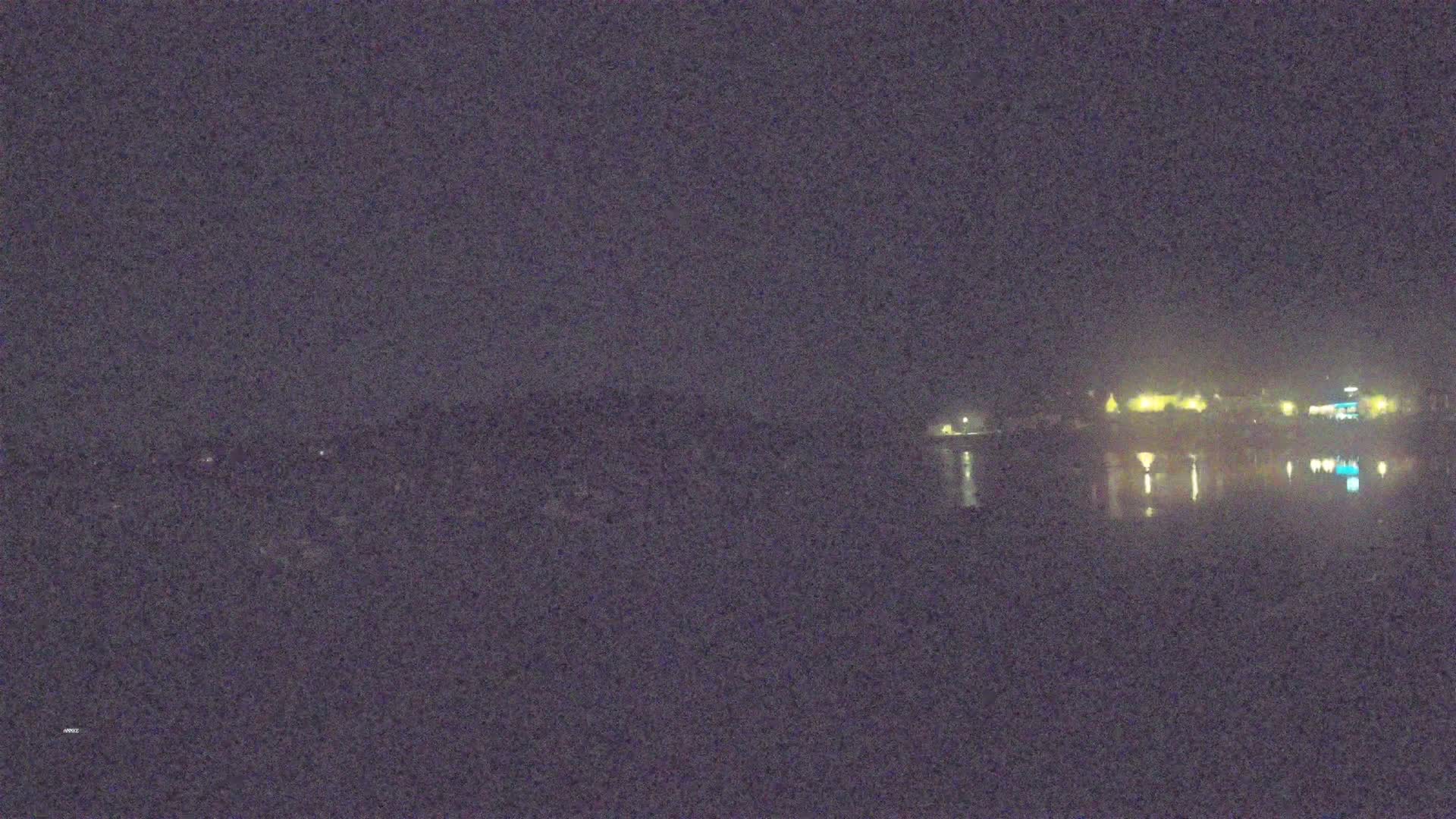 A nighttime view of dimly lit buildings across a calm body of water under a dark sky.