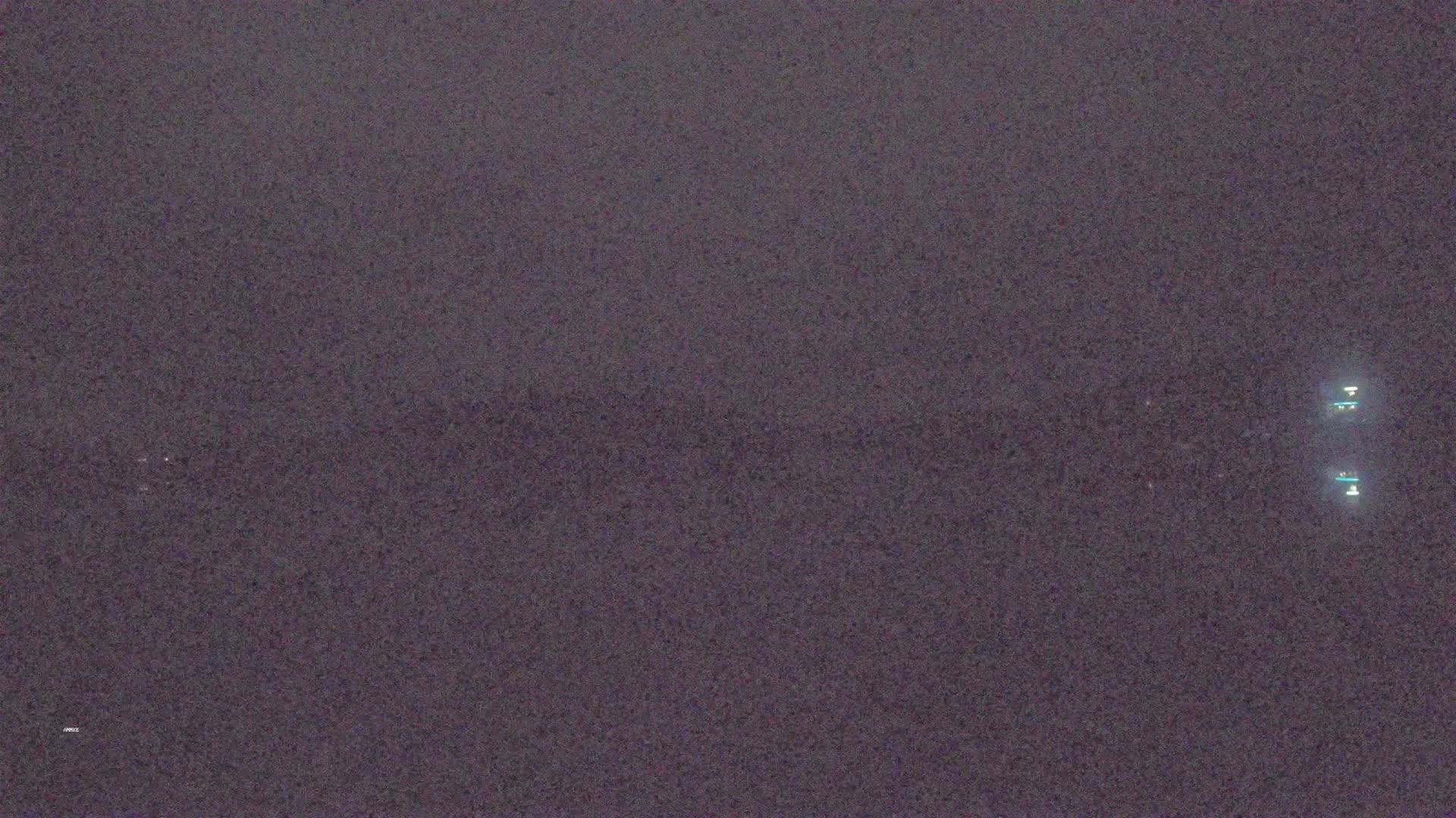 A dark, possibly nighttime, image shows a blurry, indistinct landscape with a few faint lights in the distance.