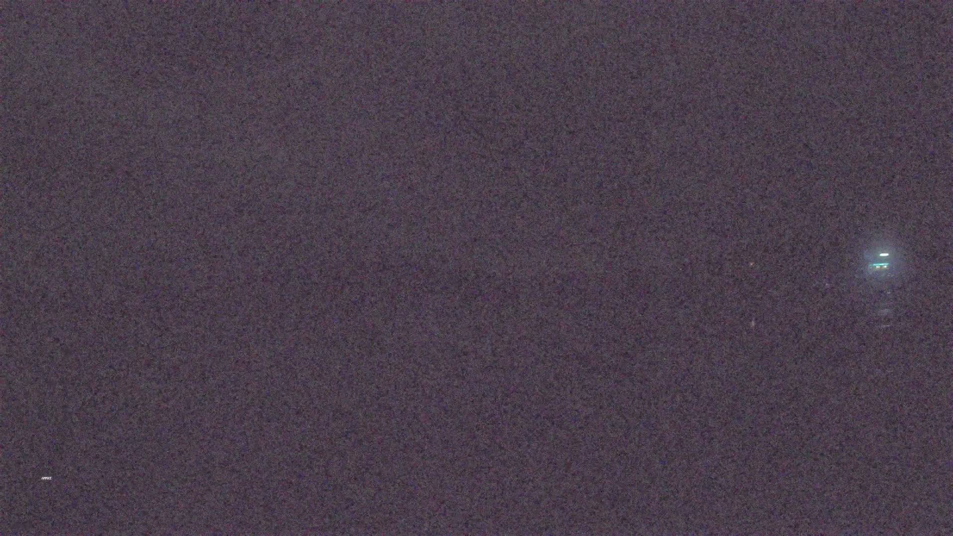 A dimly lit, dark-gray landscape is visible at night with a faint light source in the distance.