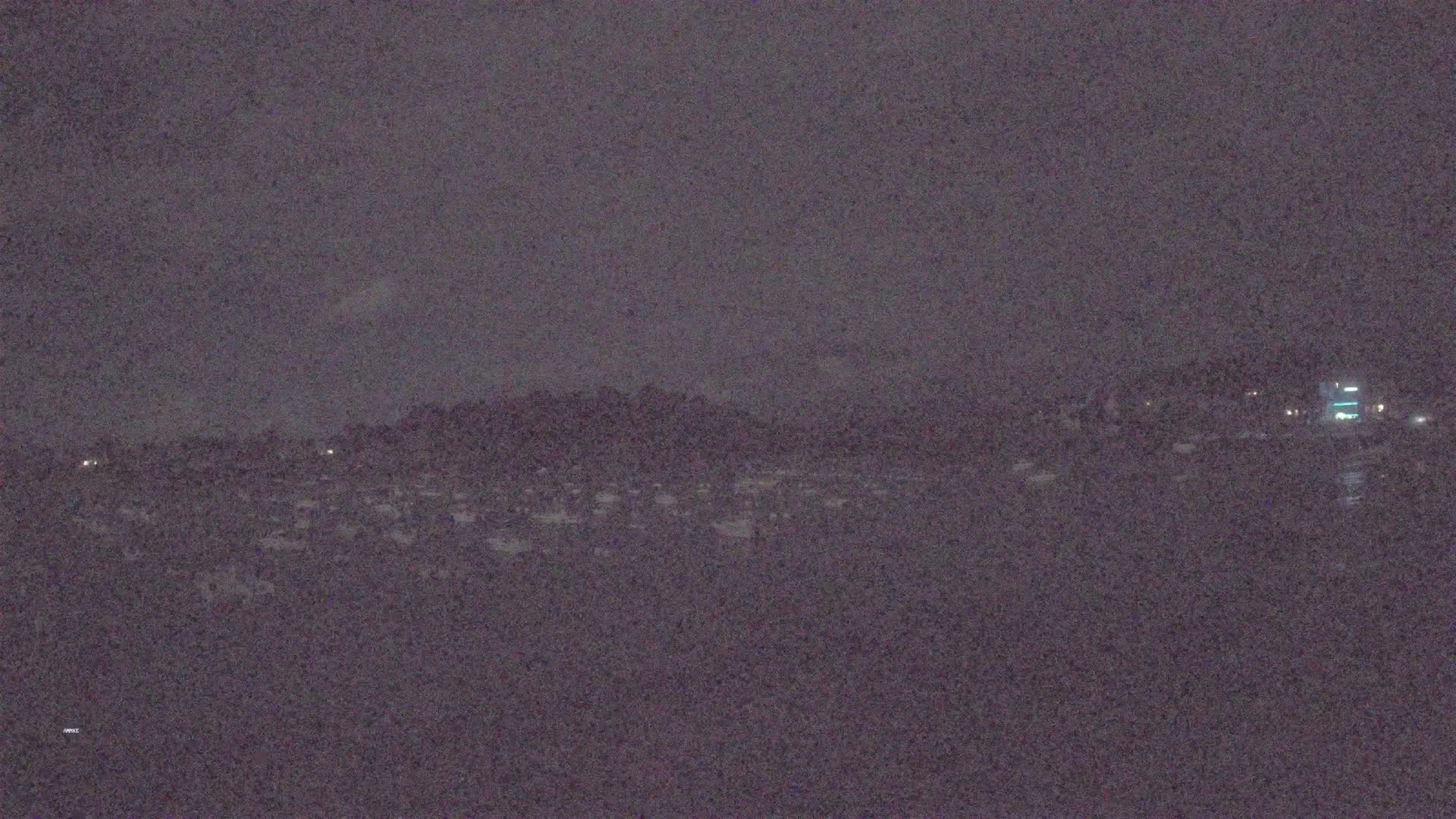 A dark, nighttime view shows a distant shoreline with faint lights under a cloudy sky.