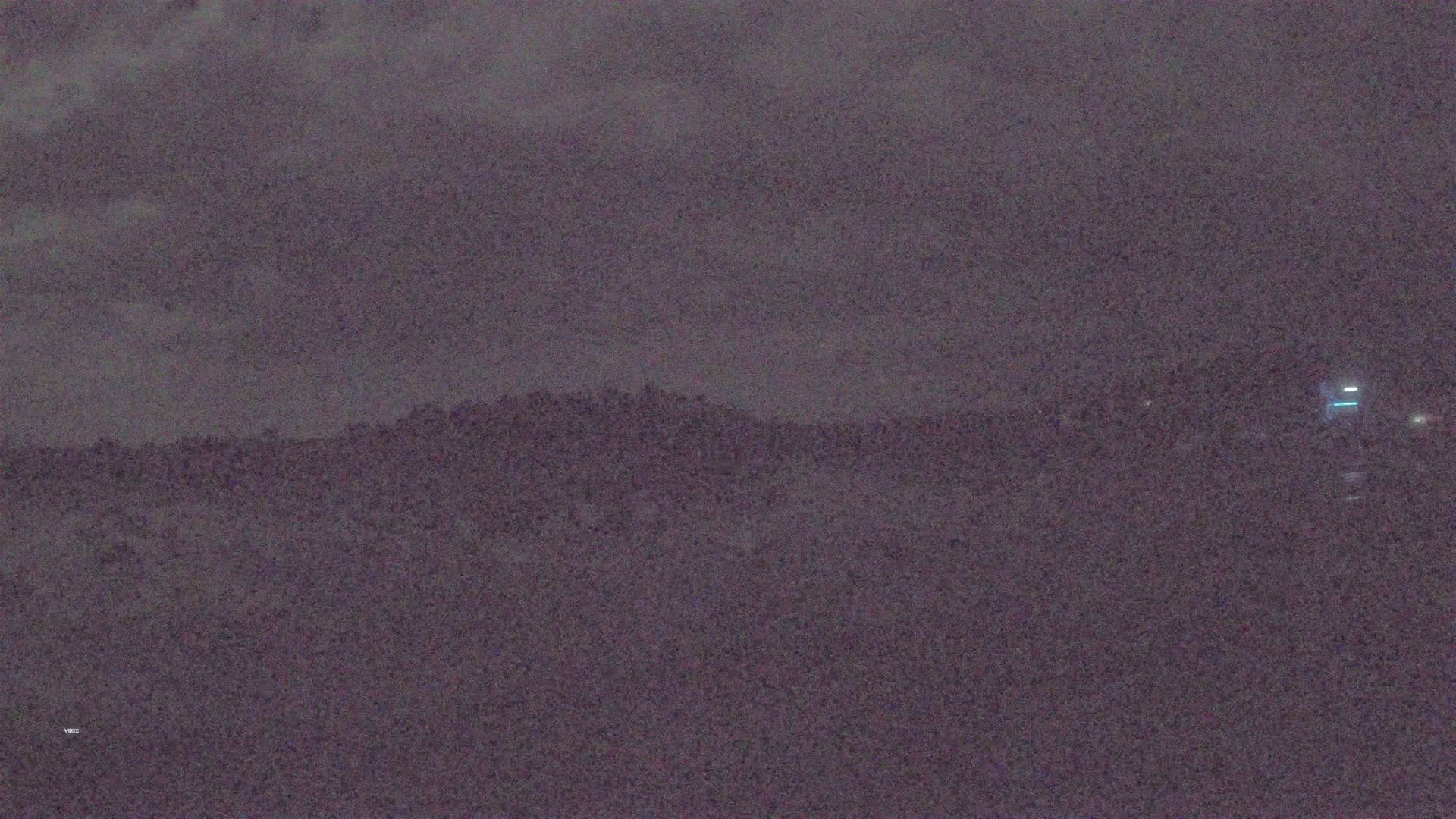 A dark, overcast nighttime scene shows a distant, silhouetted hill line.