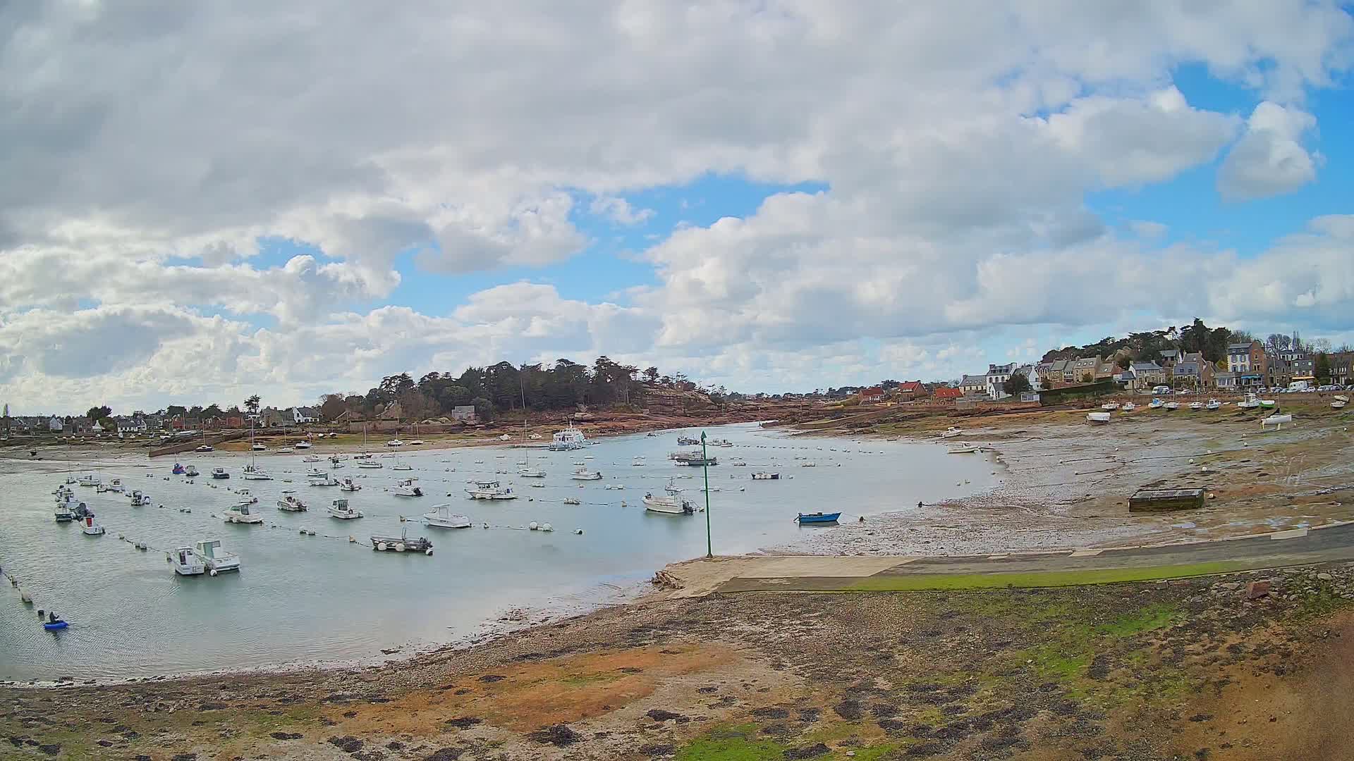 Numerous small boats are moored in a calm harbor, partially exposed at low tide under a partly cloudy sky.