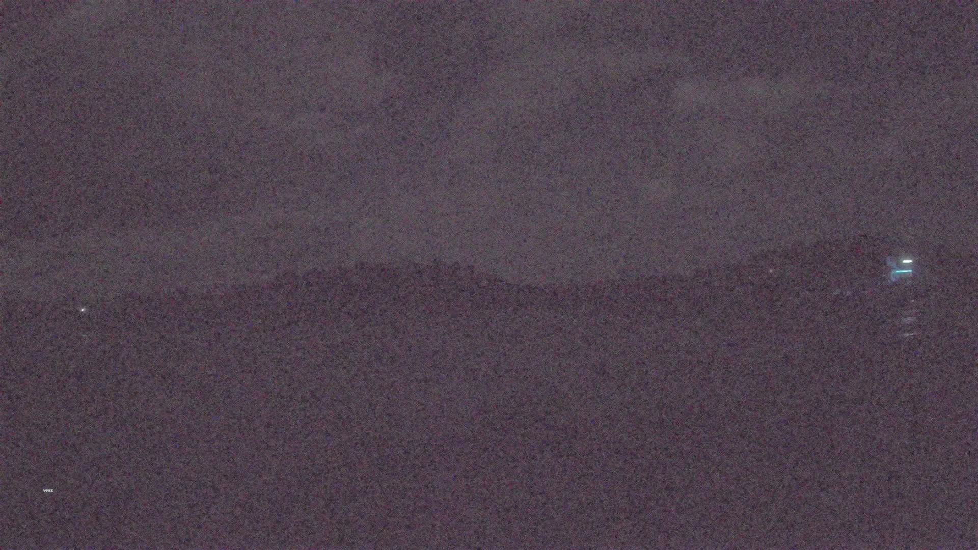 A dark, nighttime landscape shows a distant, indistinct shoreline under a cloudy sky.