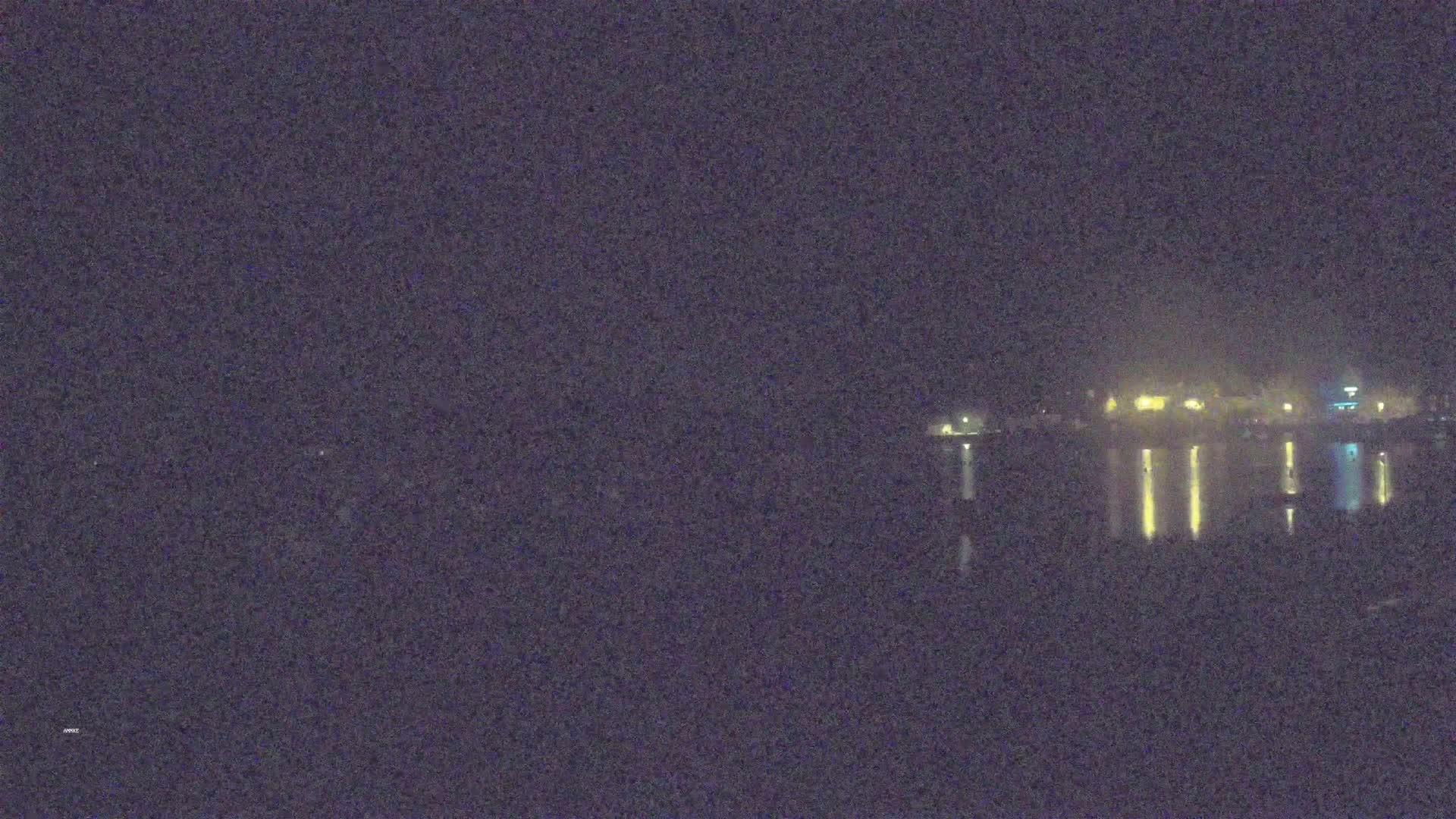 A nighttime, hazy view of a body of water reflecting the lights of buildings across the shore.
