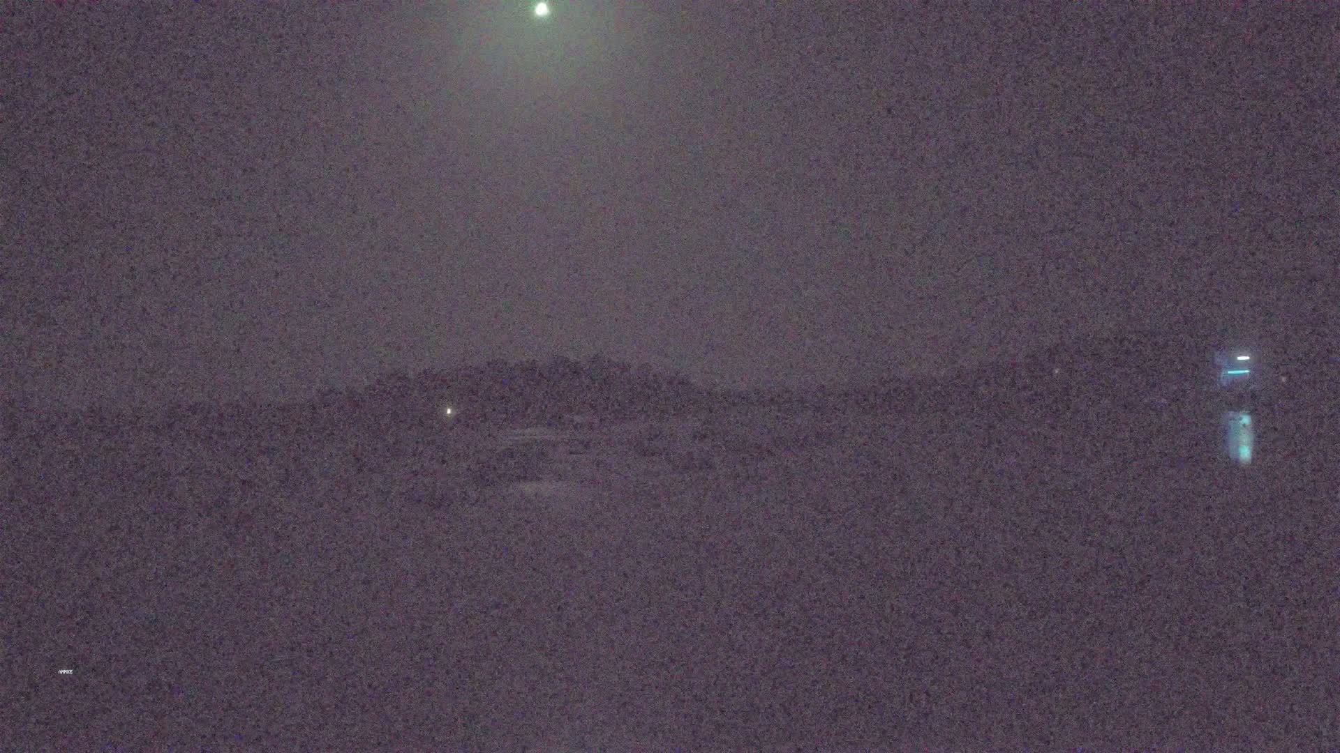 A dark, possibly nighttime, outdoor scene shows a dimly lit landscape under a hazy sky with a bright light source in the upper center.