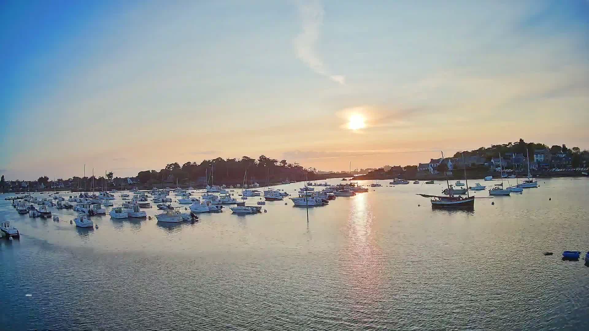 Many small boats are moored in a calm harbor at sunset under a clear sky.