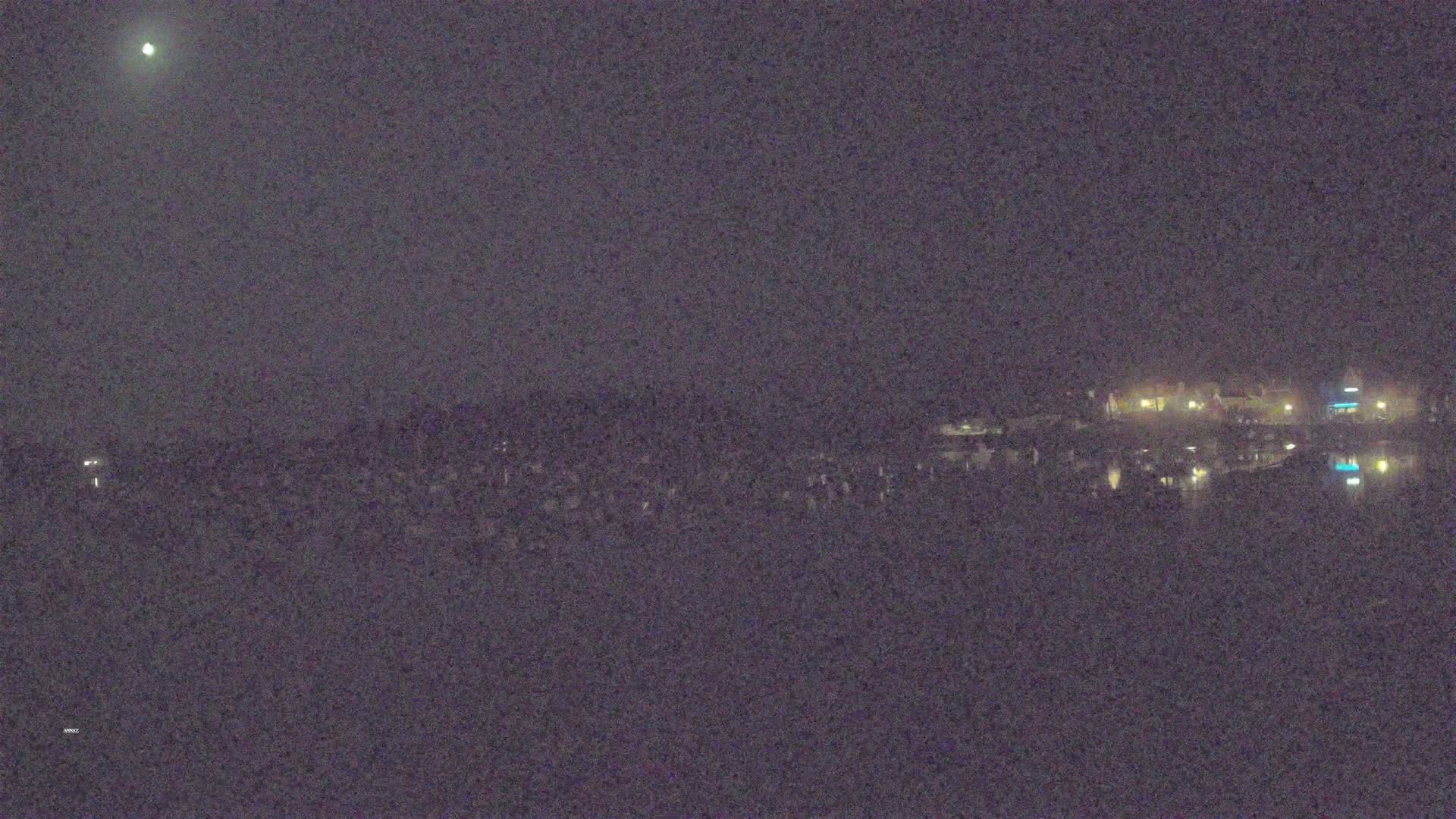 A nighttime long shot shows a body of water reflecting the lights of buildings on the far shore under a dark, moonlit sky.
