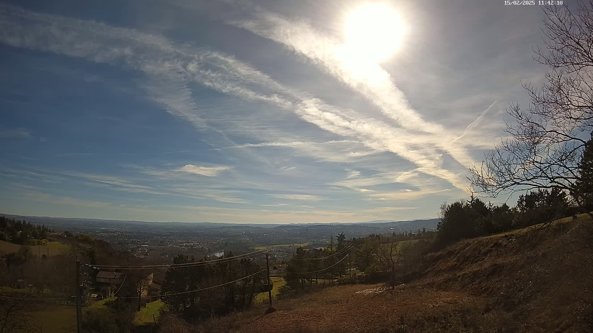 A sunny day with wispy cirrus clouds overhead reveals a panoramic view of a valley town nestled among rolling hills and distant mountains.